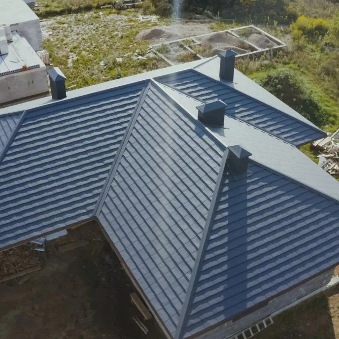 Aerial view of a blue metal roof with multiple chimneys on a house in a grassy area