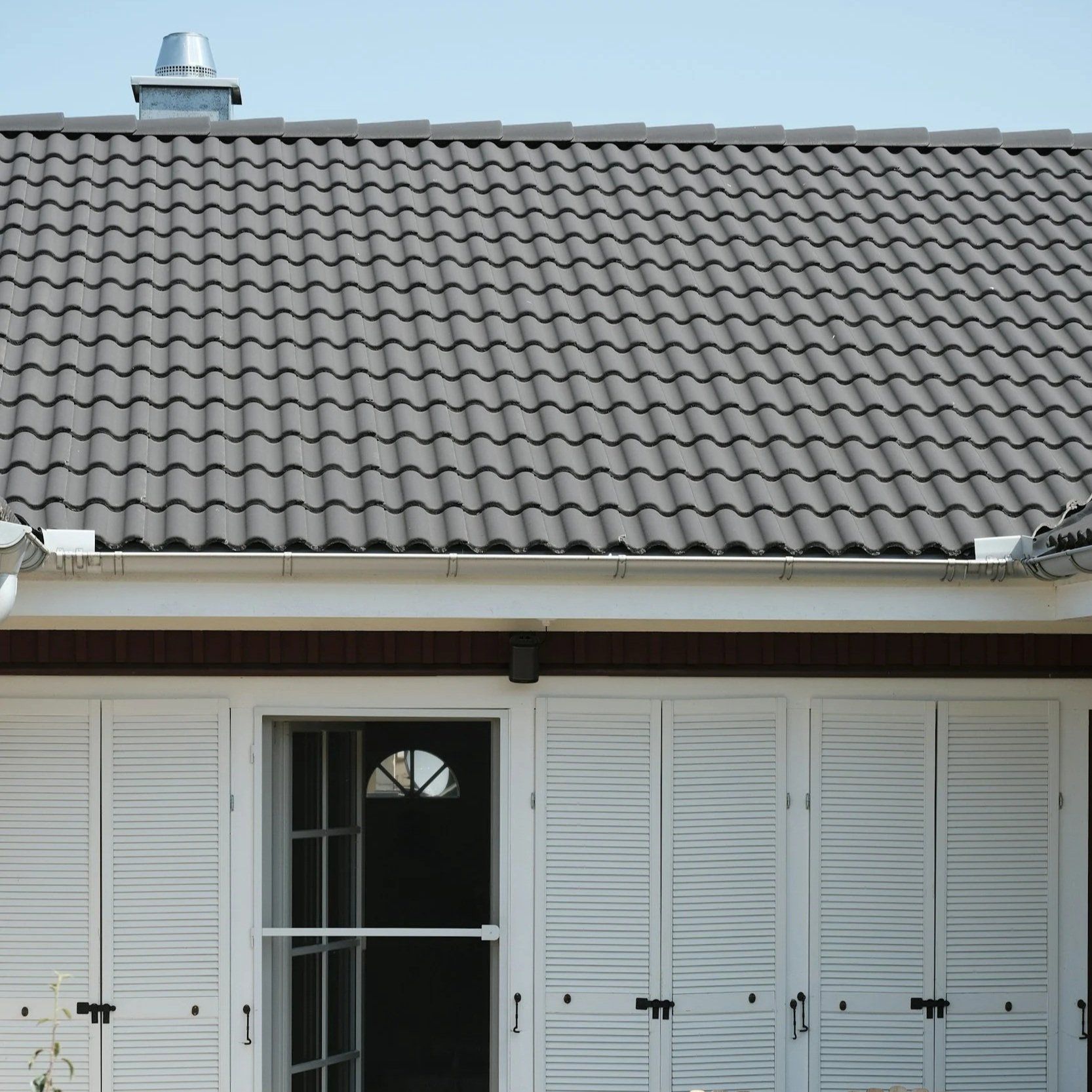 White shuttered house facade with a gray tiled roof and centered doorway