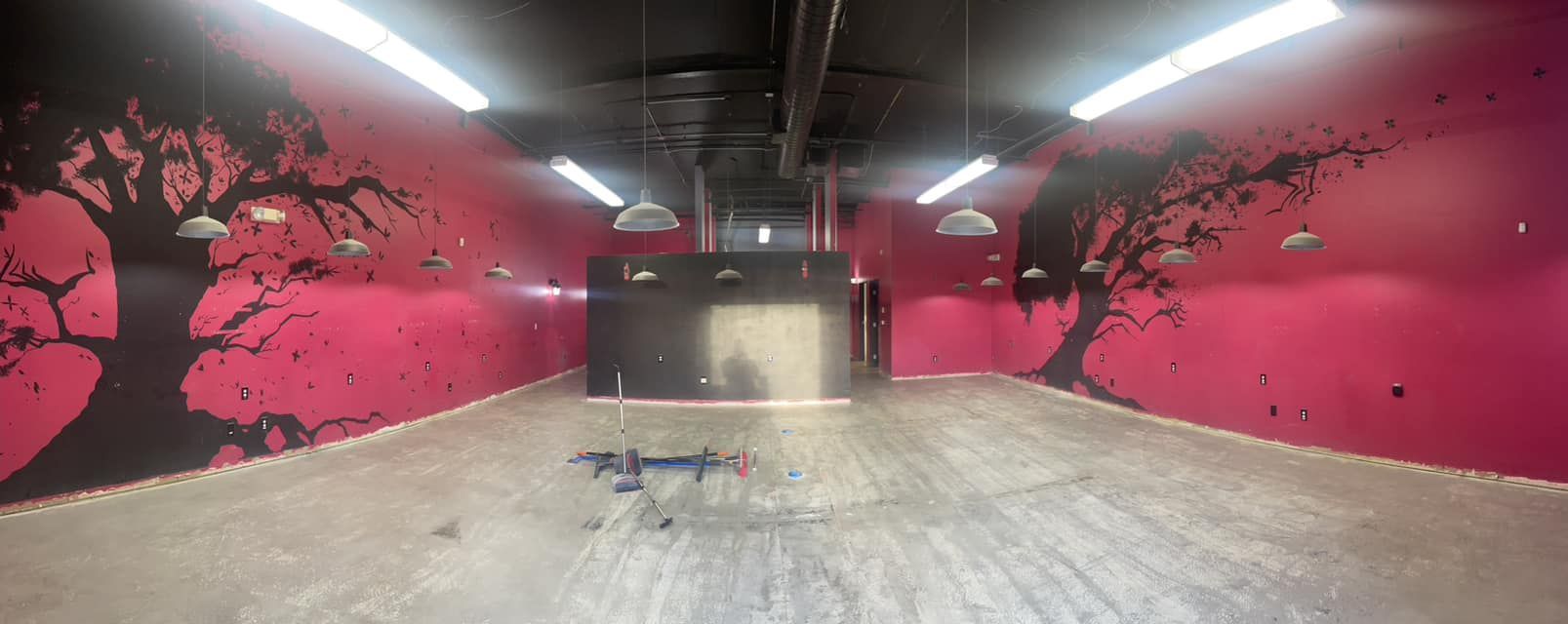 A small, blue drone flies inside a pink room with black tree murals on the walls.