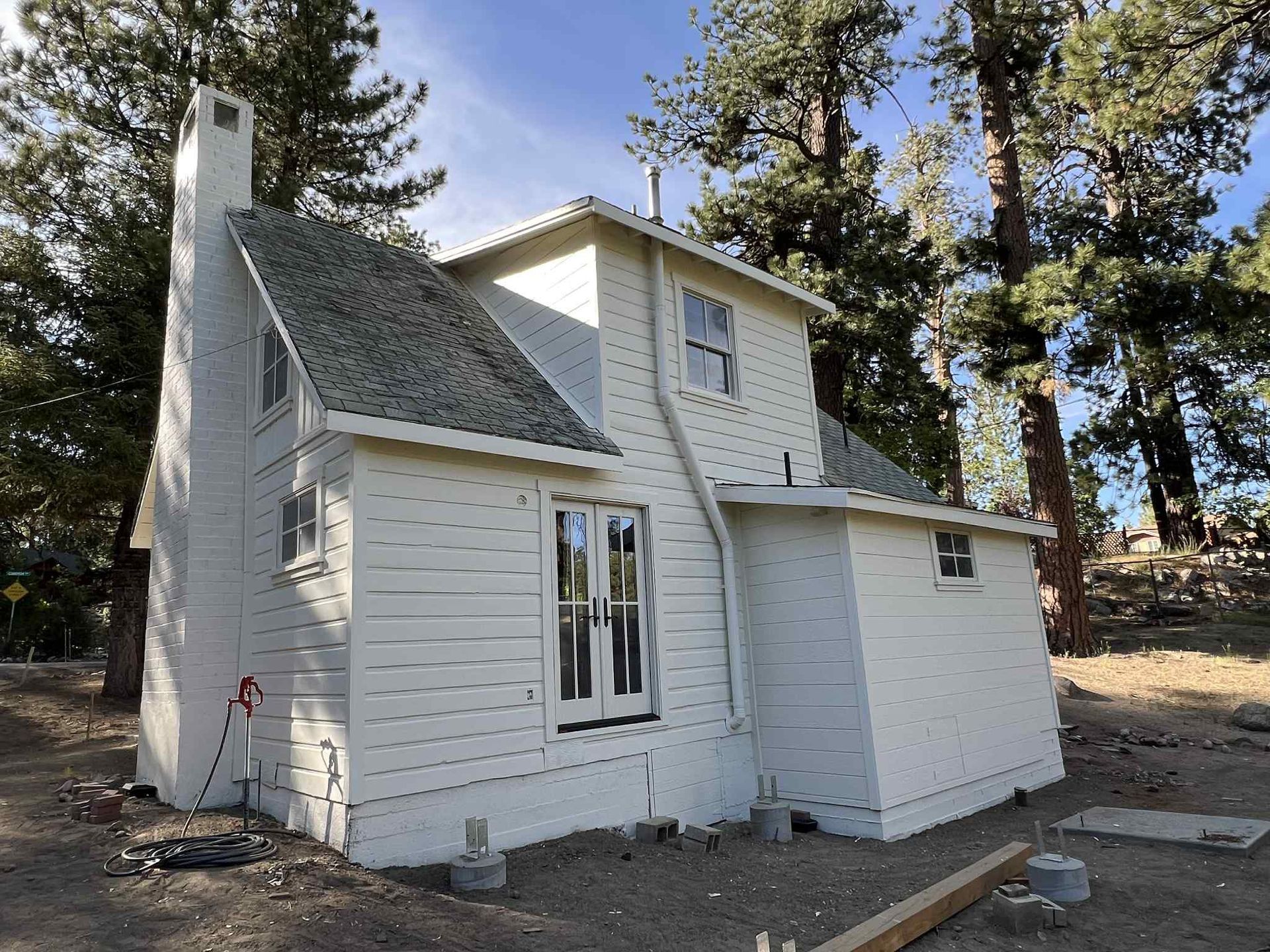 White house with a tall chimney, surrounded by trees, set in a dirt yard.