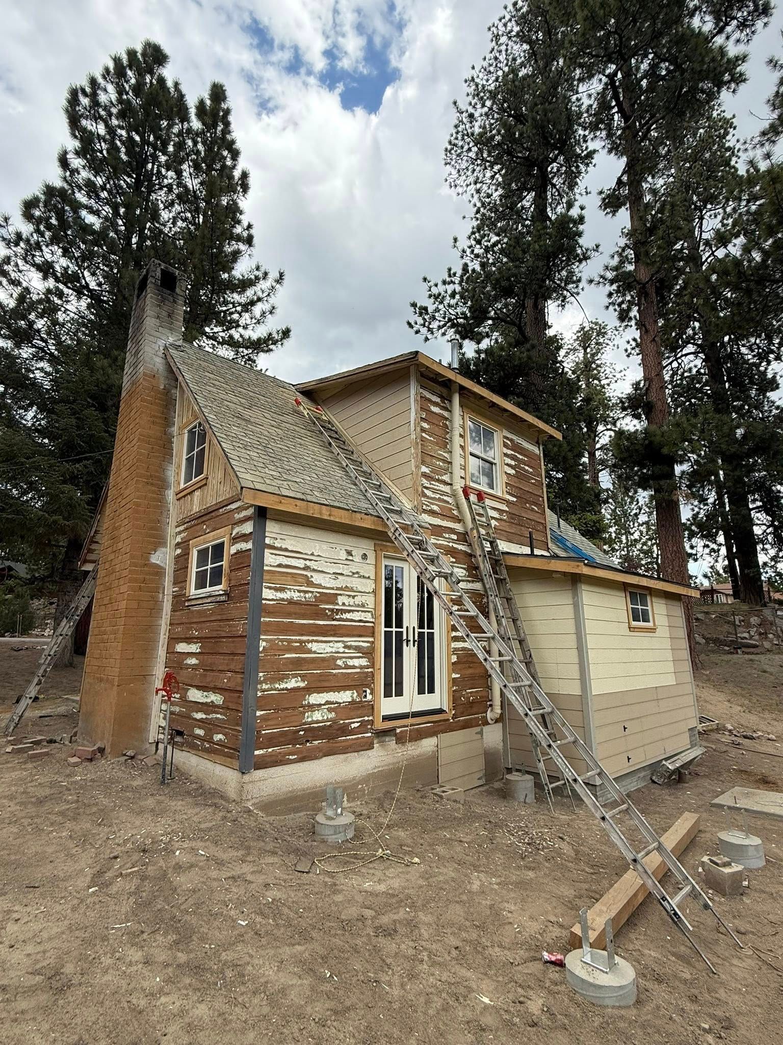 House under construction; brown and beige exterior, tall brick chimney. Ladder leans against the side.