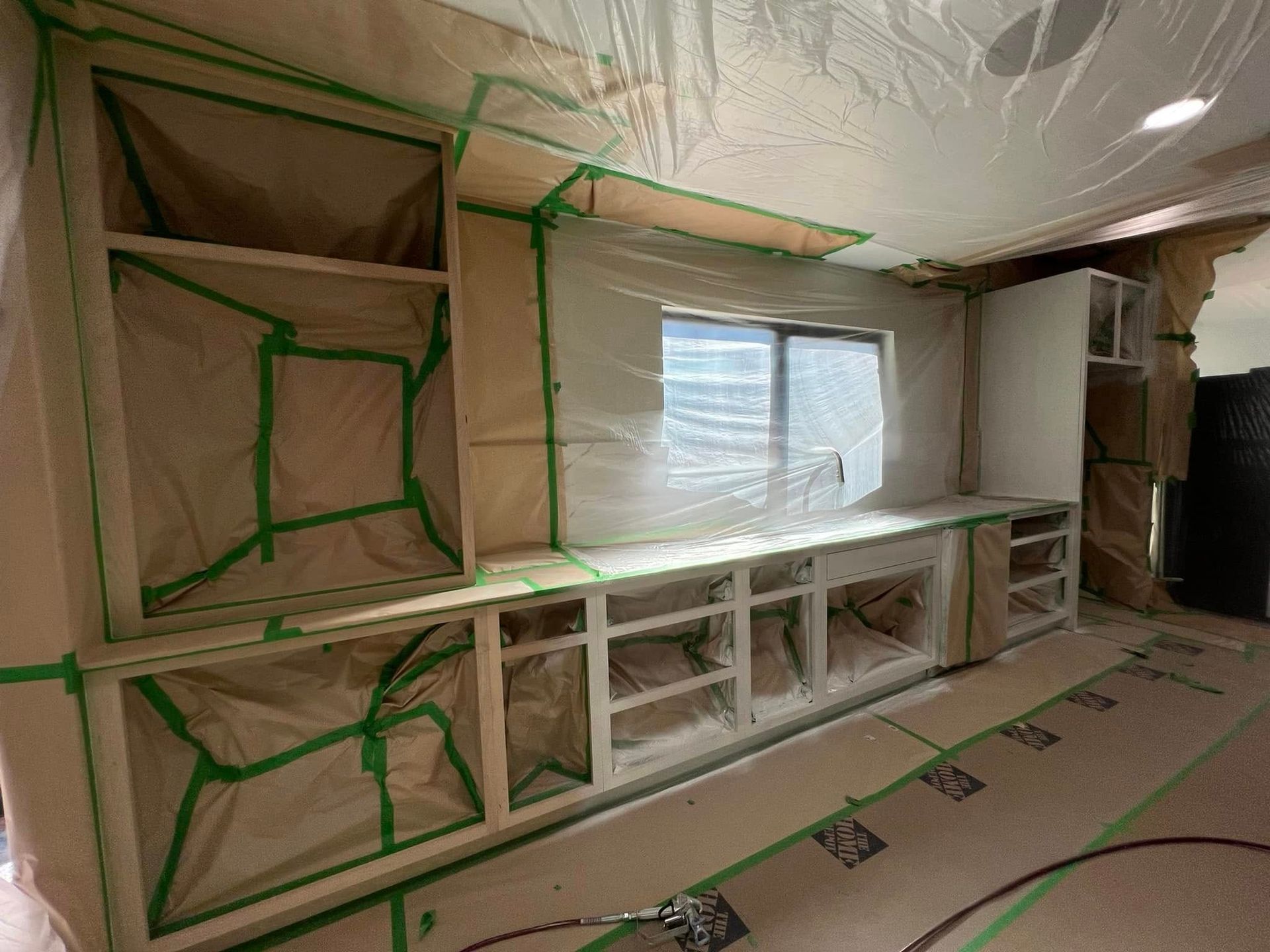Kitchen cabinets covered in plastic and tape, prepped for painting.