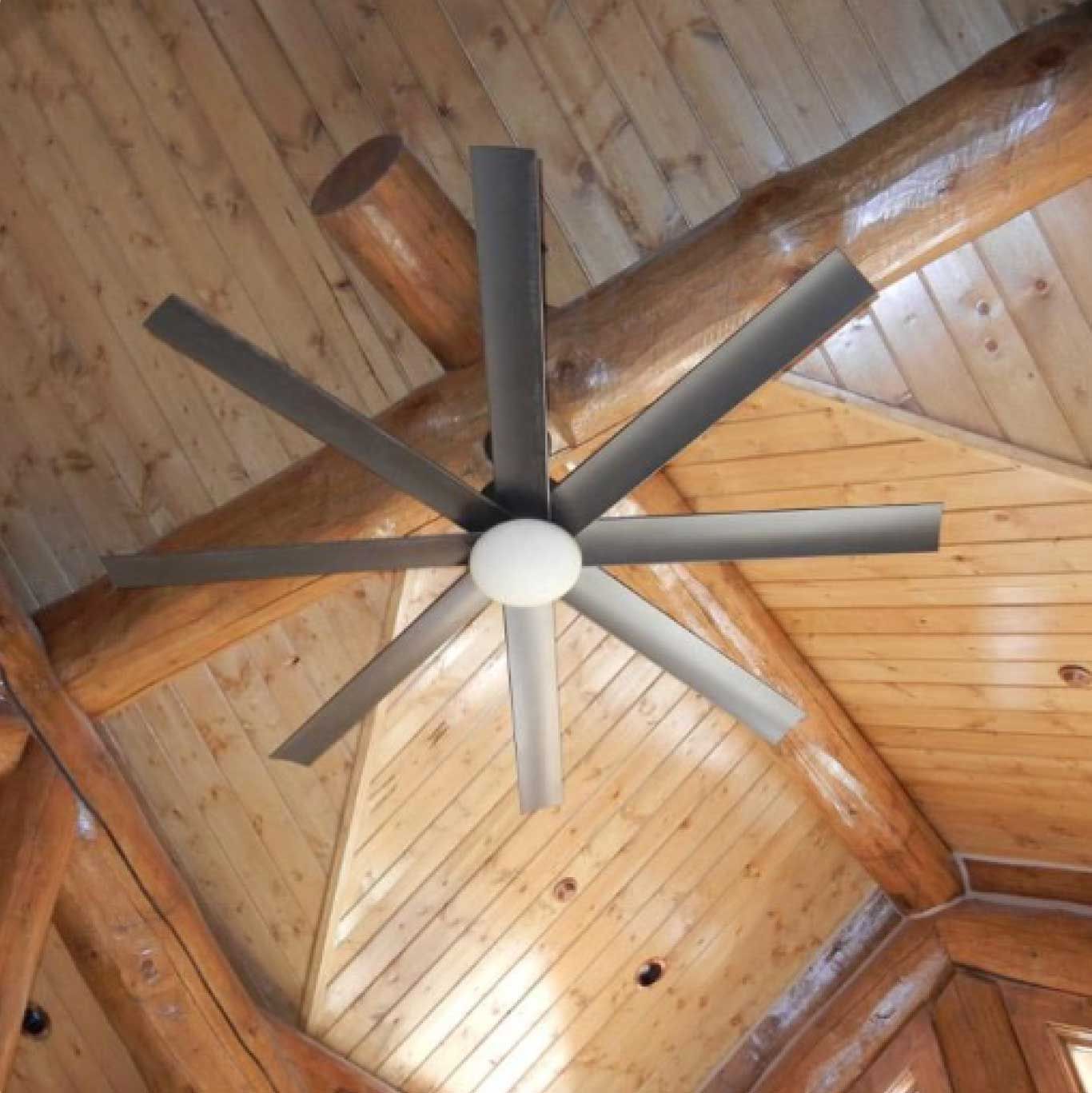 Ceiling fan with eight gray blades and a white globe light in a wooden cabin.