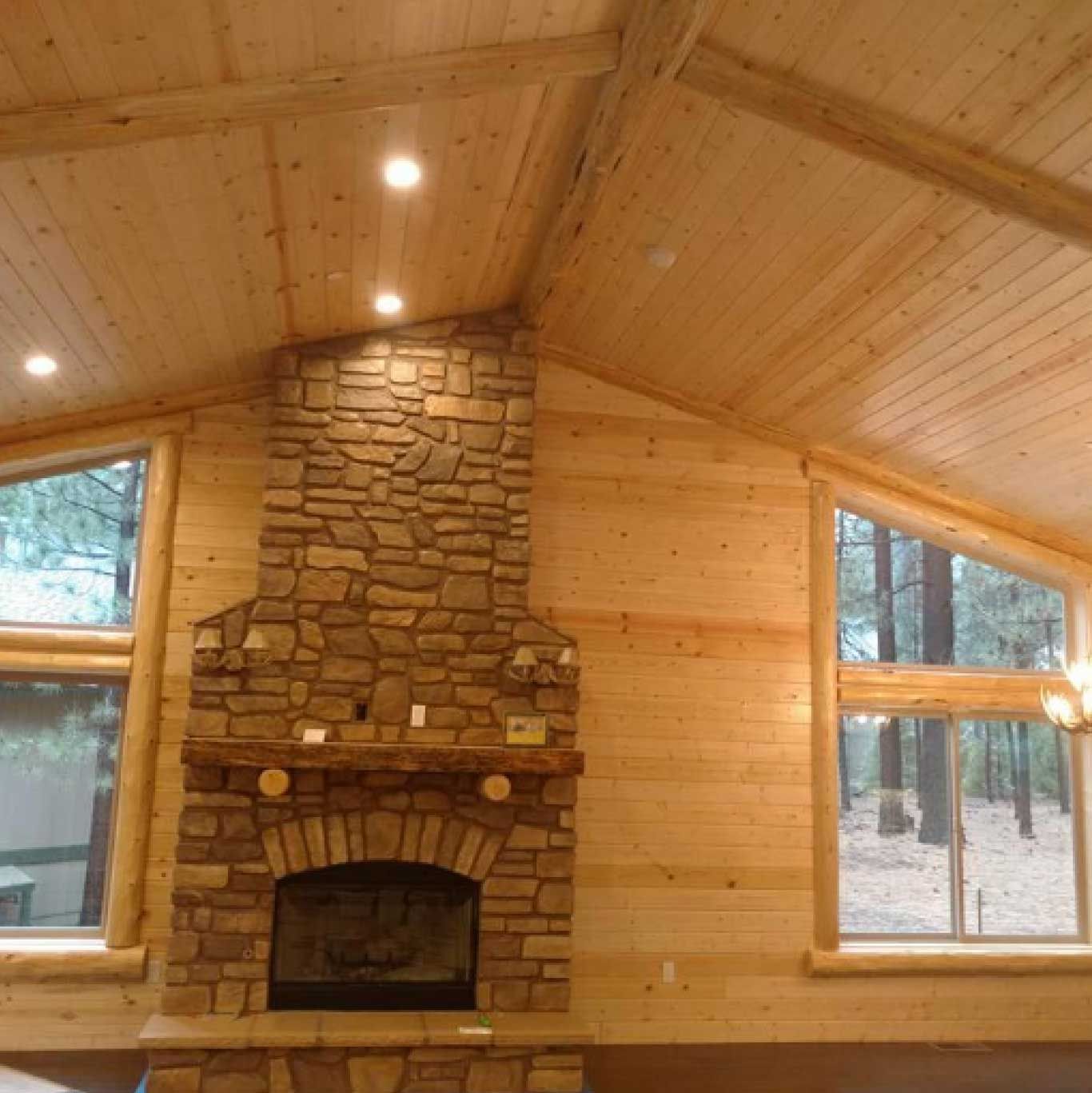 Stone fireplace in a wood-paneled room with large windows and a high, angled ceiling.