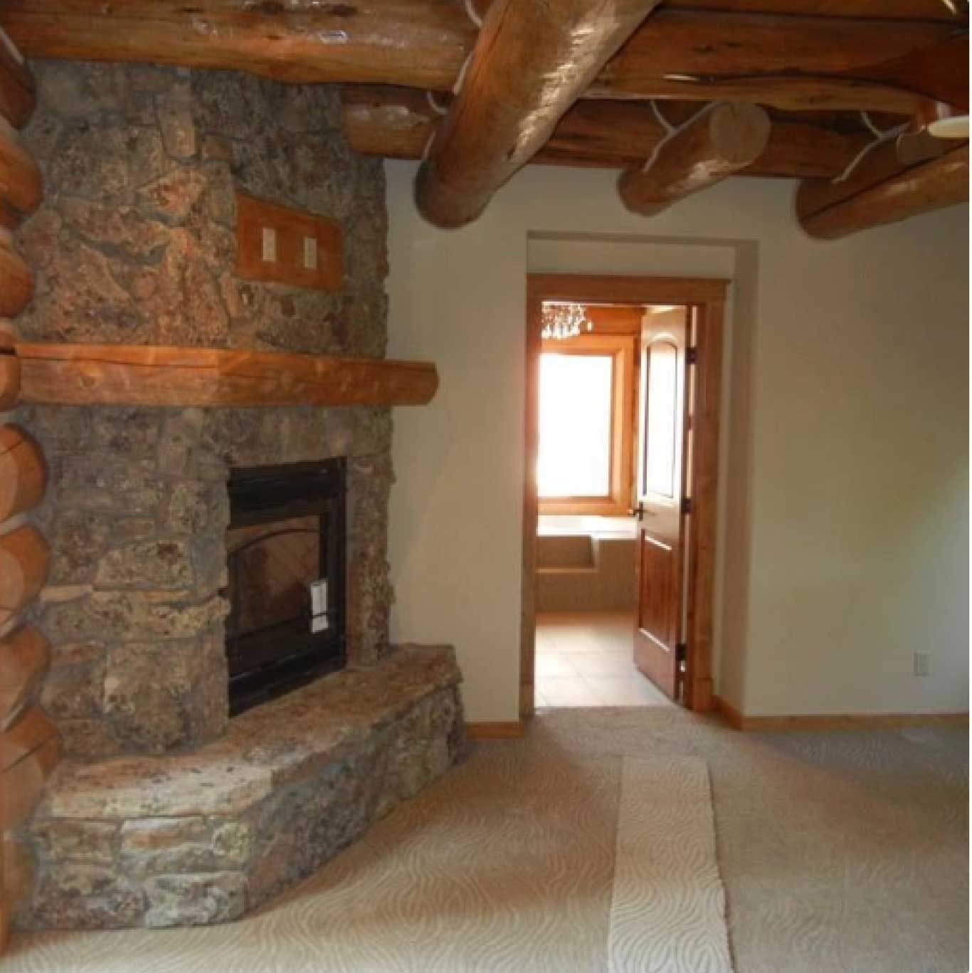 Stone fireplace in a log cabin living room; doorway leads to bathroom.