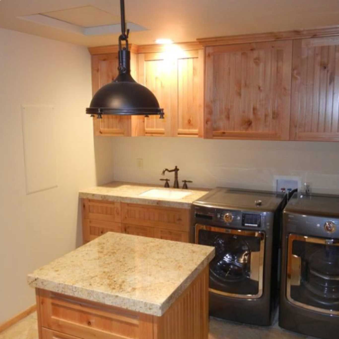 Laundry room with wood cabinets, granite countertop, and dark washer and dryer; black pendant light.