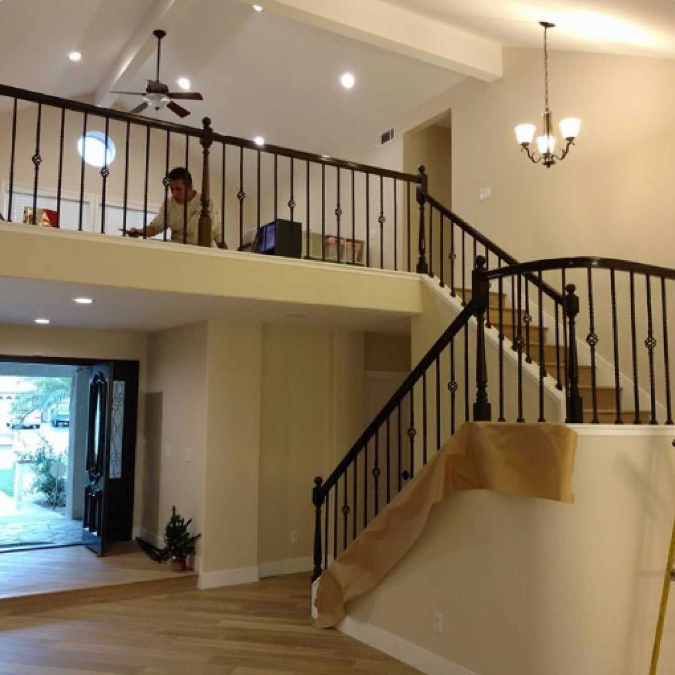 A spacious two-story home interior with a staircase, balcony, and a person standing upstairs.