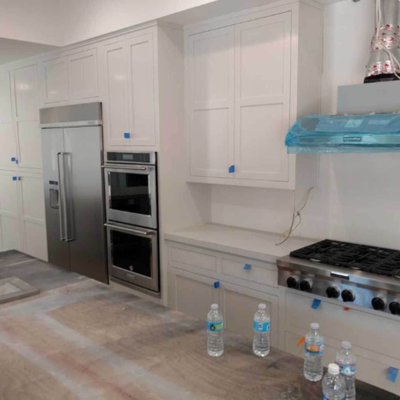 Newly installed white kitchen cabinets with stainless steel appliances; still under construction.