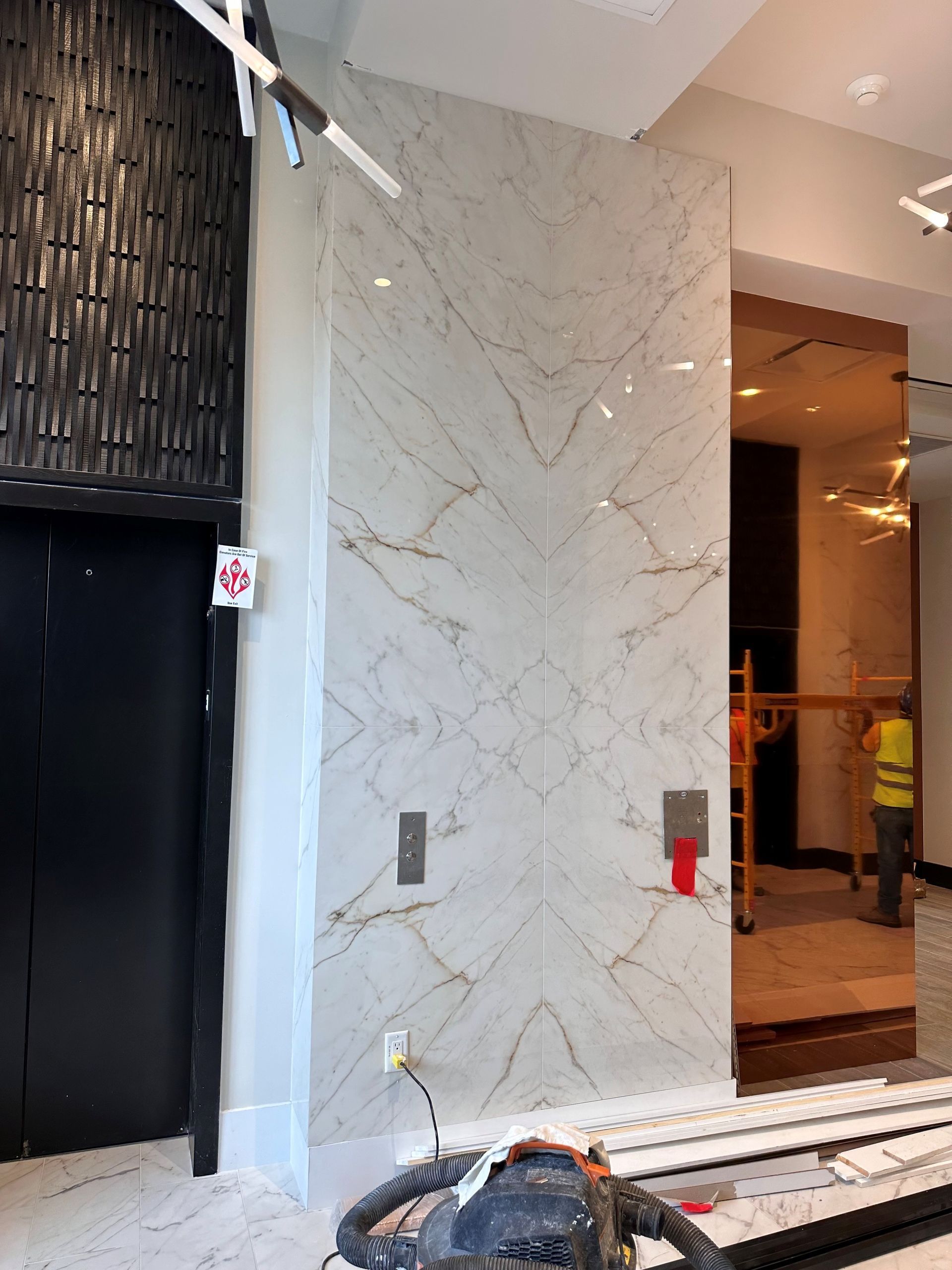 A man in a yellow vest is standing in front of a marble wall.
