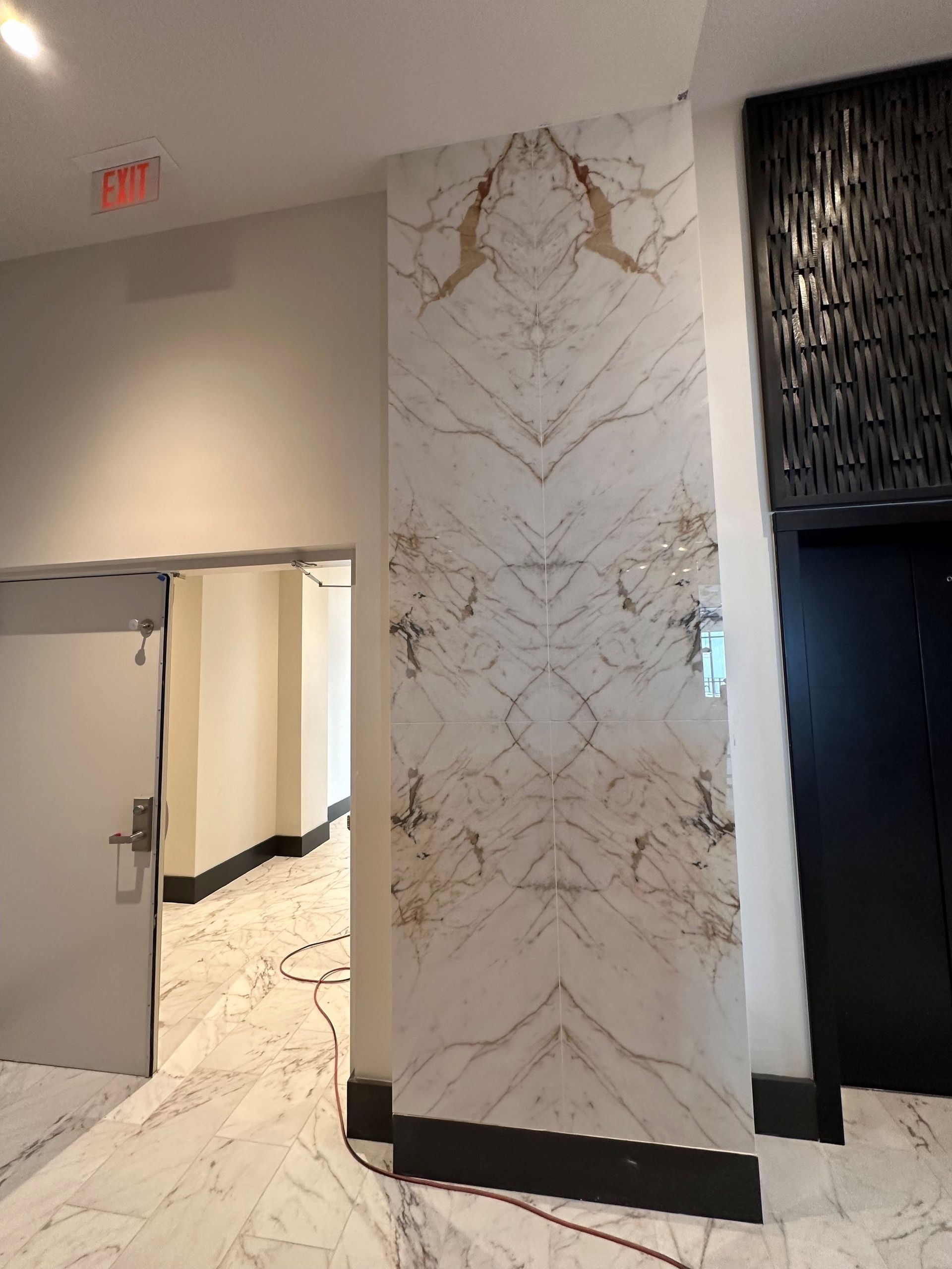 A hallway with a marble wall and a black door