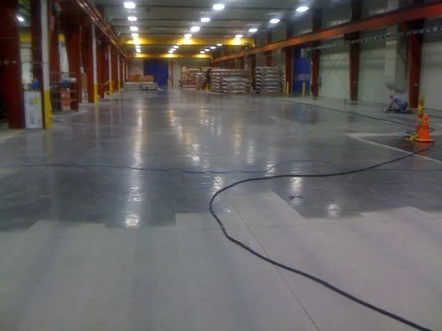 A large warehouse with a concrete floor being painted