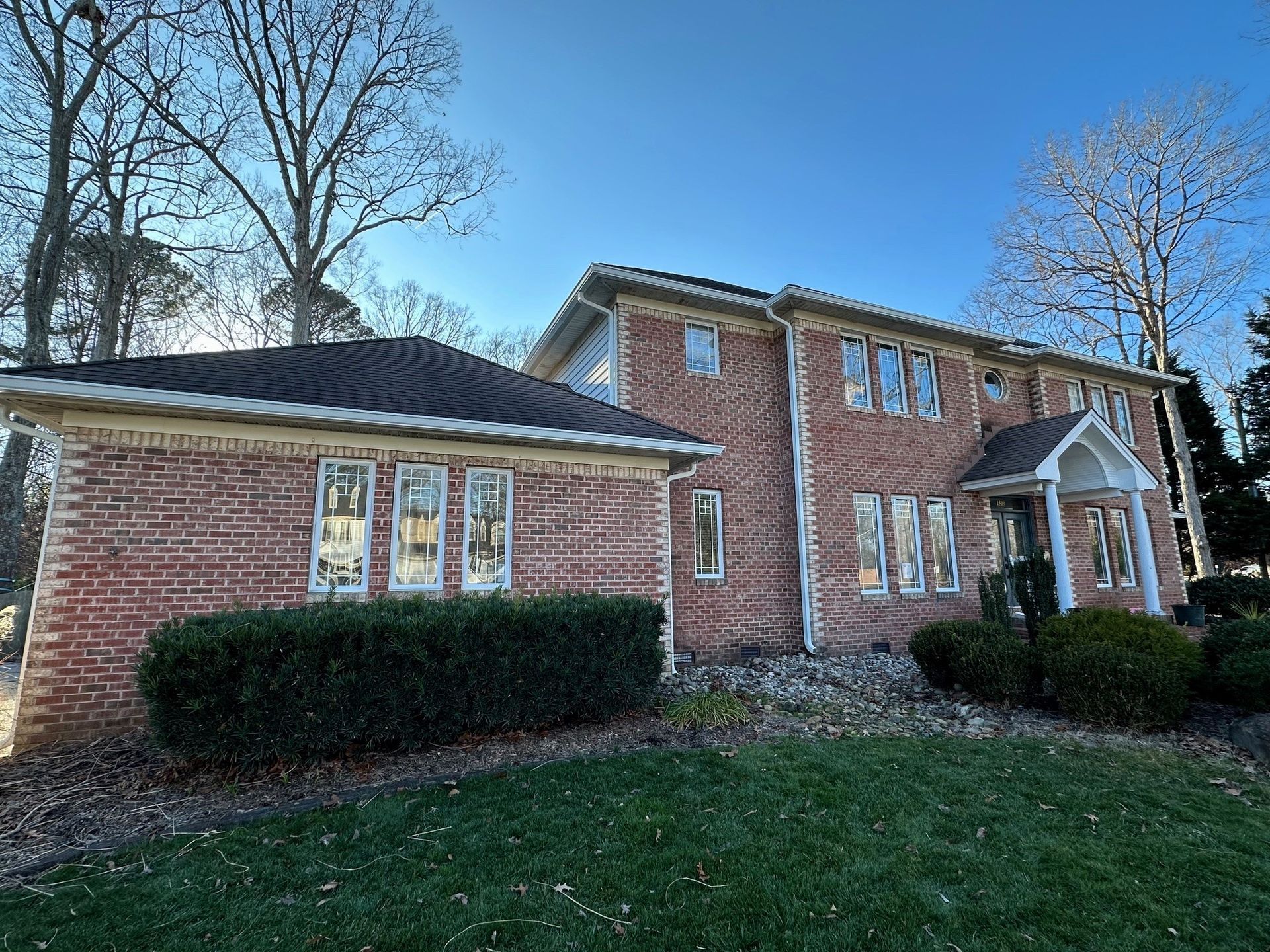 Red brick house with dark roof and green lawn on a sunny day.