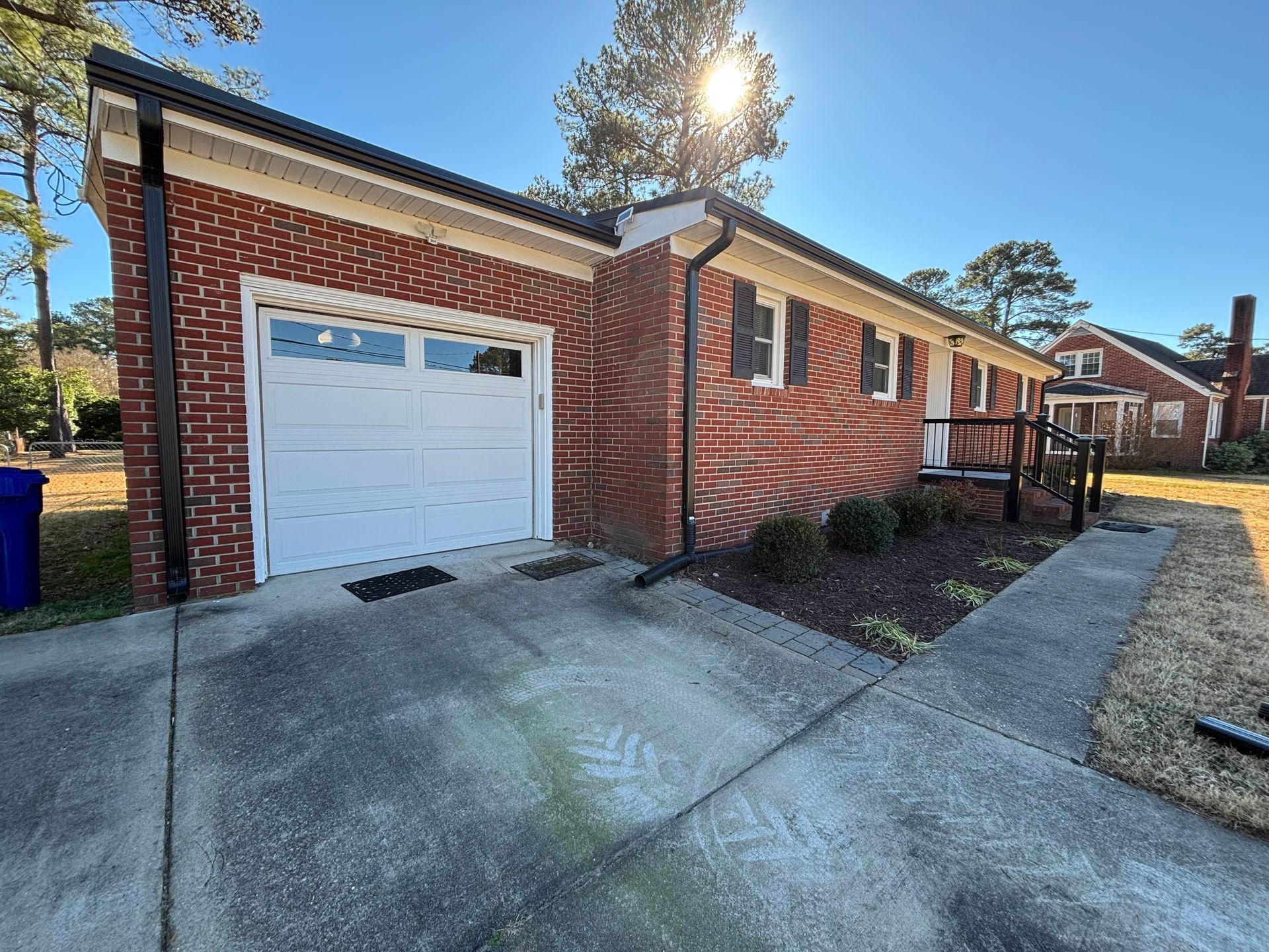 Brick house with a garage and black trim. Concrete driveway and sidewalk.