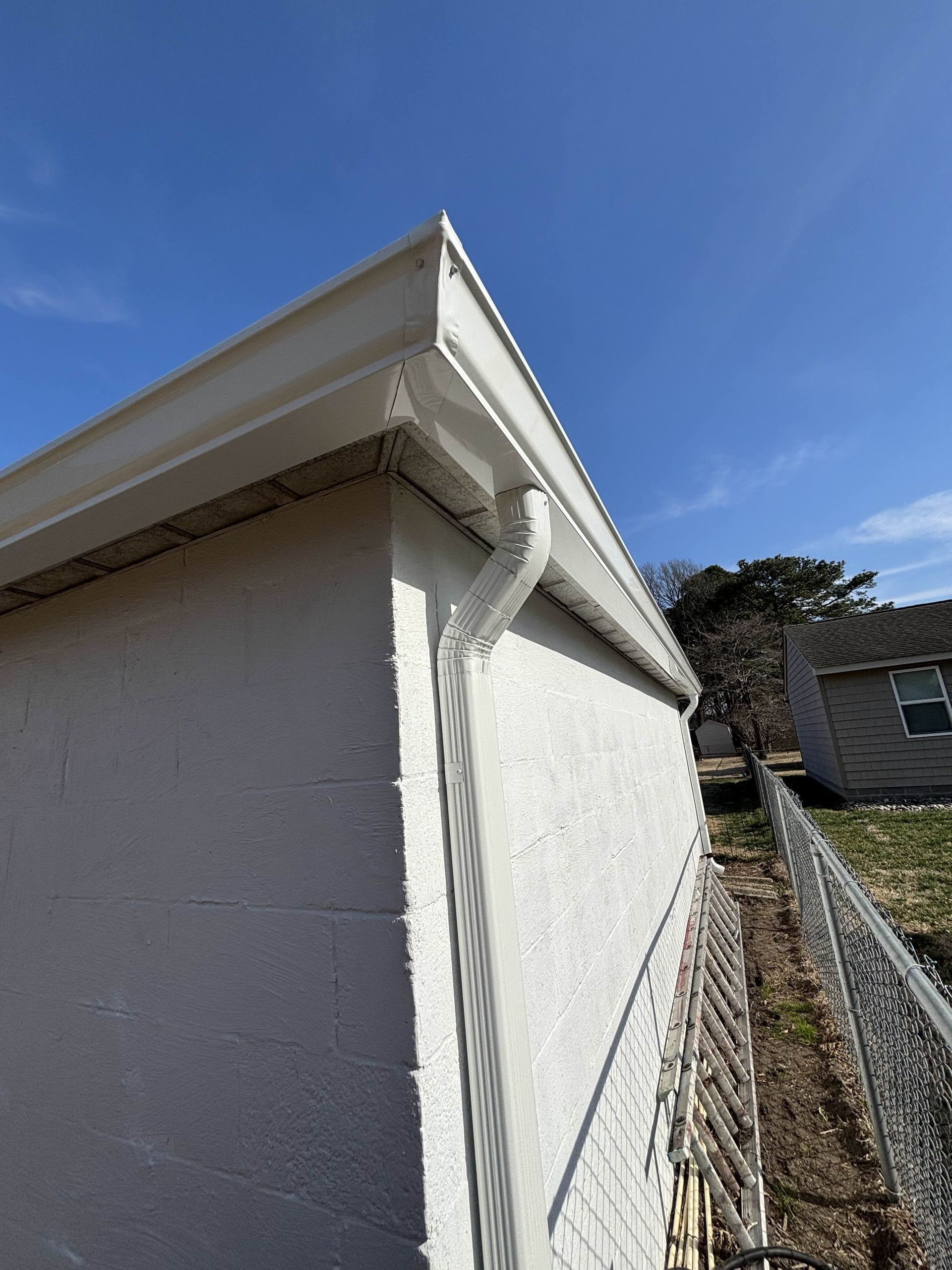 White building corner with guttering, against a blue sky.