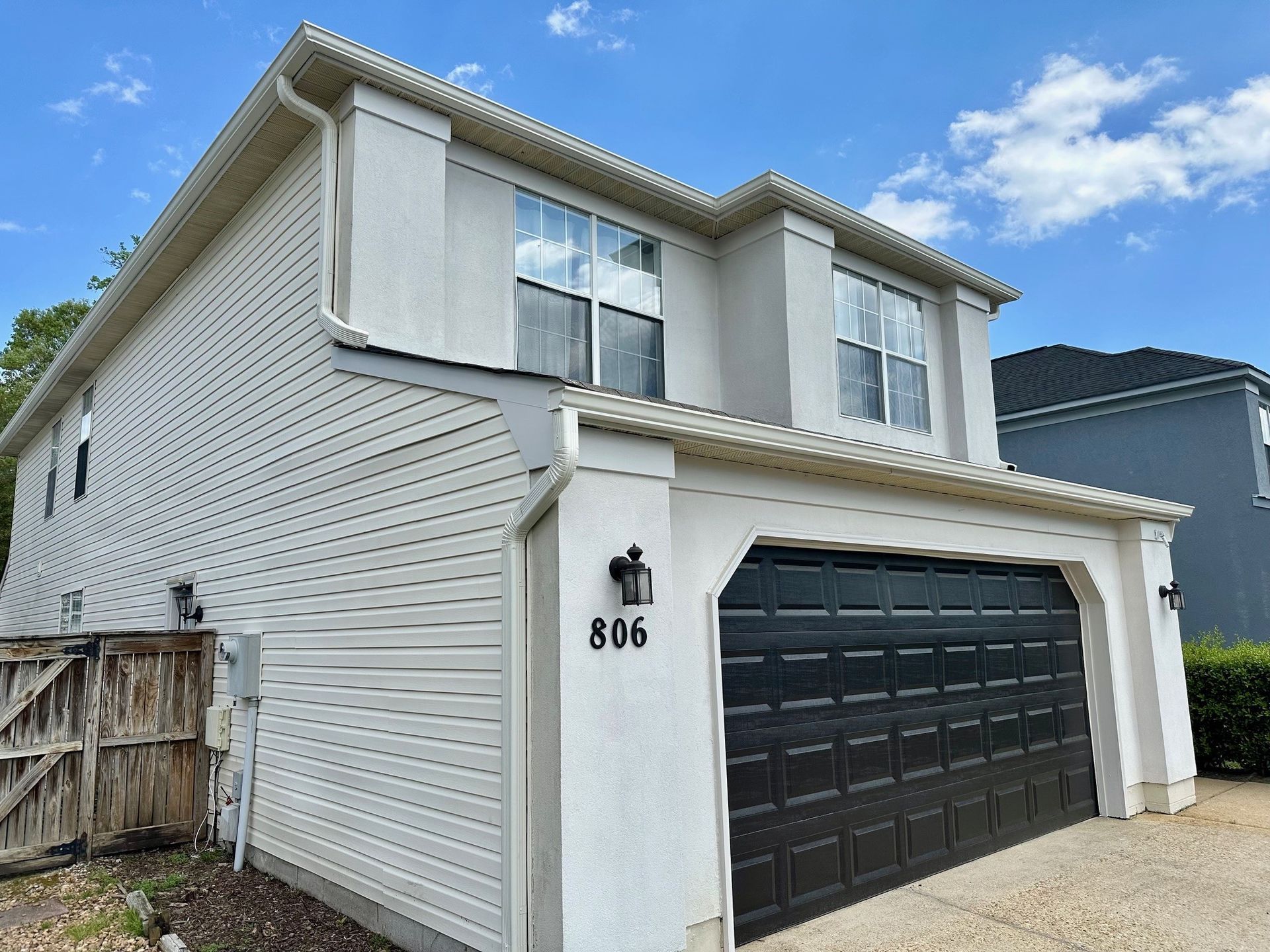 Two-story house with white siding and garage, black garage door, and a light blue sky.