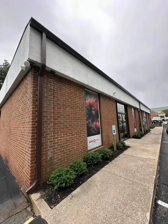 Brick commercial building with brown trim, sidewalk, and landscaping.