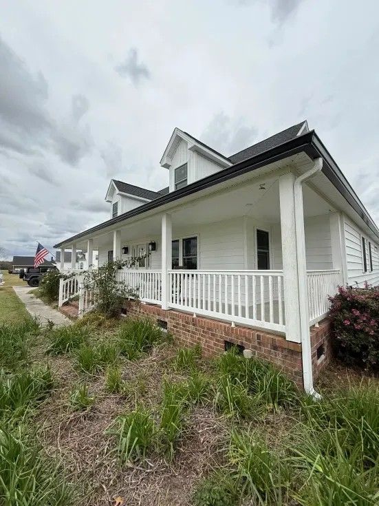 White house with a porch and railings, surrounded by grass and a cloudy sky.