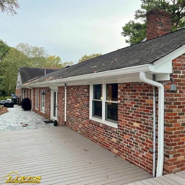 Brick house with white trim, gutters, and a gray deck. Overcast day.