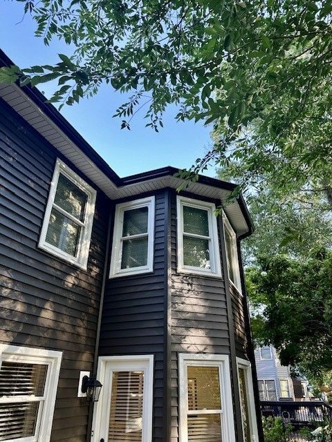 Dark wood-paneled house with white-framed windows, under a blue sky and tree branches.