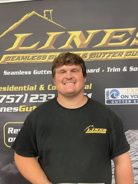 A smiling man in a black shirt stands in front of a business sign about gutters.