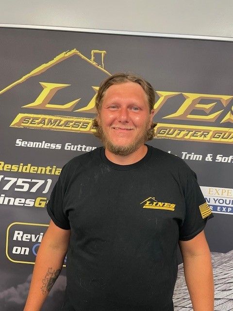 Man in black shirt smiles in front of a company sign, 
