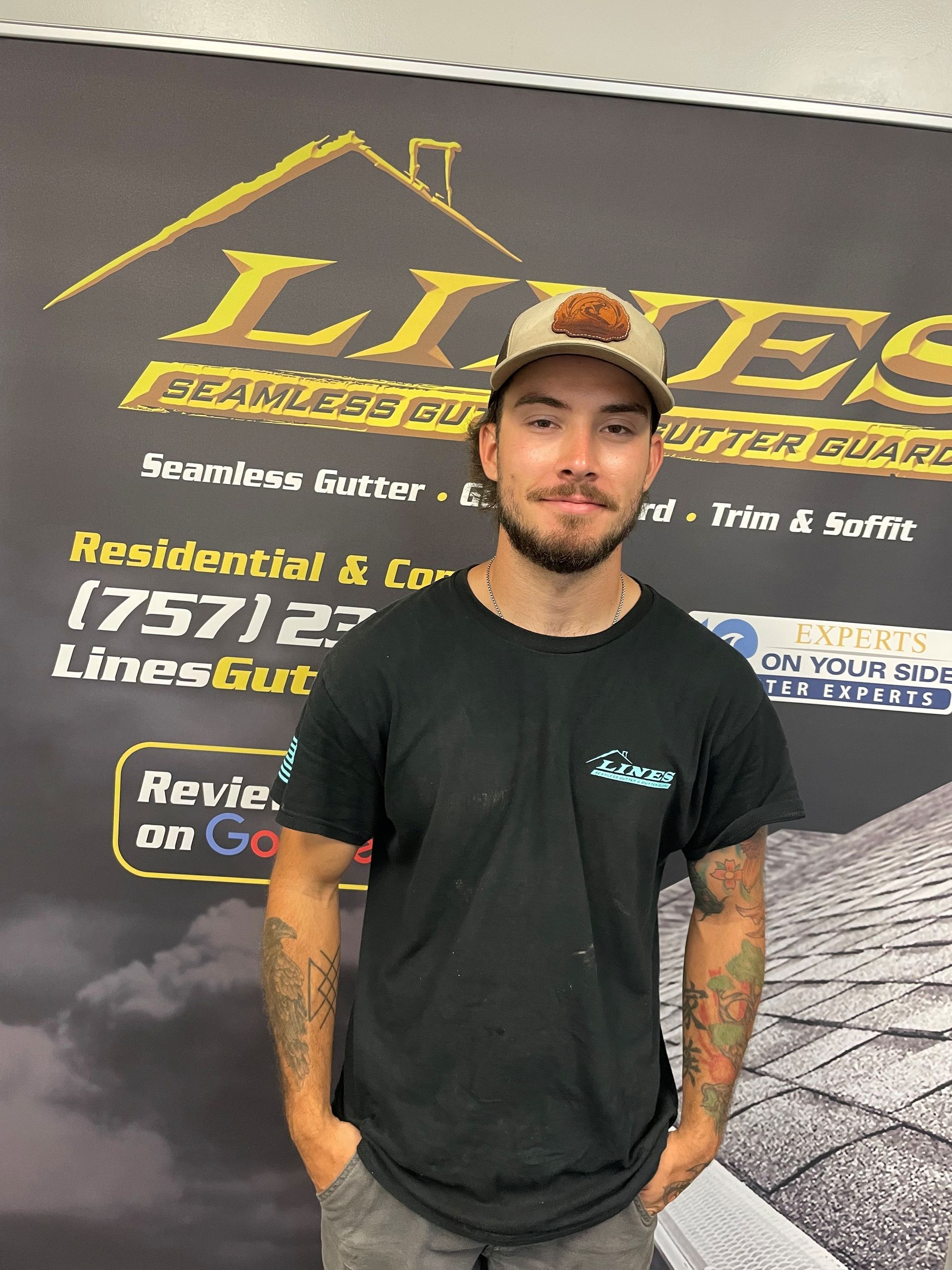 Man in front of a business sign for Lines Gutters, wearing a hat, hands in pockets.