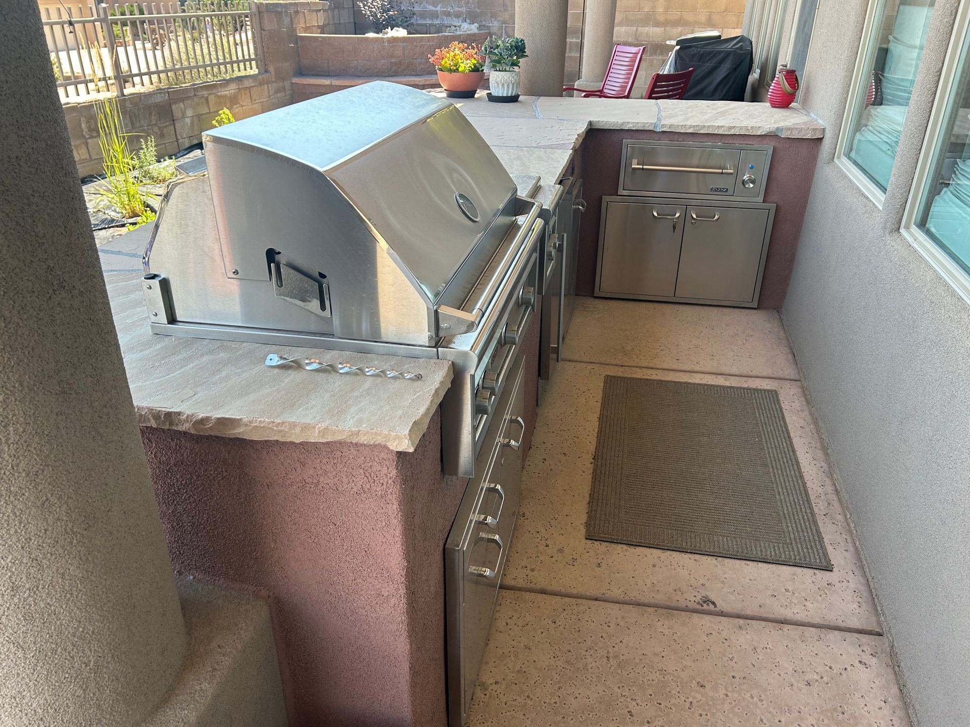 Stainless steel outdoor kitchen with grill and cabinets in a patio setting.