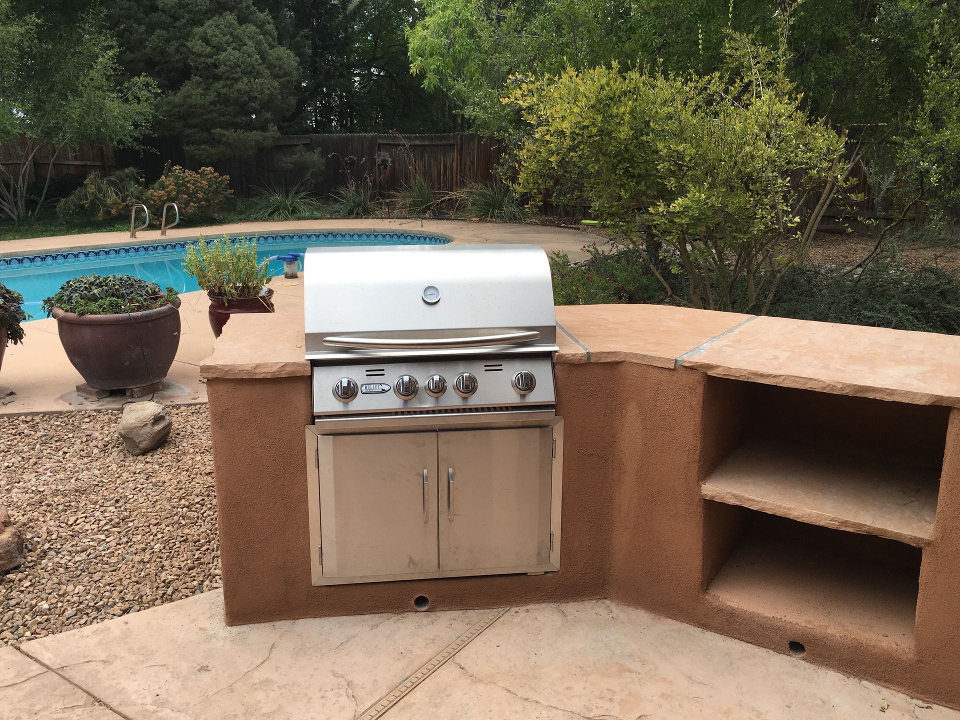 Outdoor kitchen with a grill, cabinets, and counter by a pool.