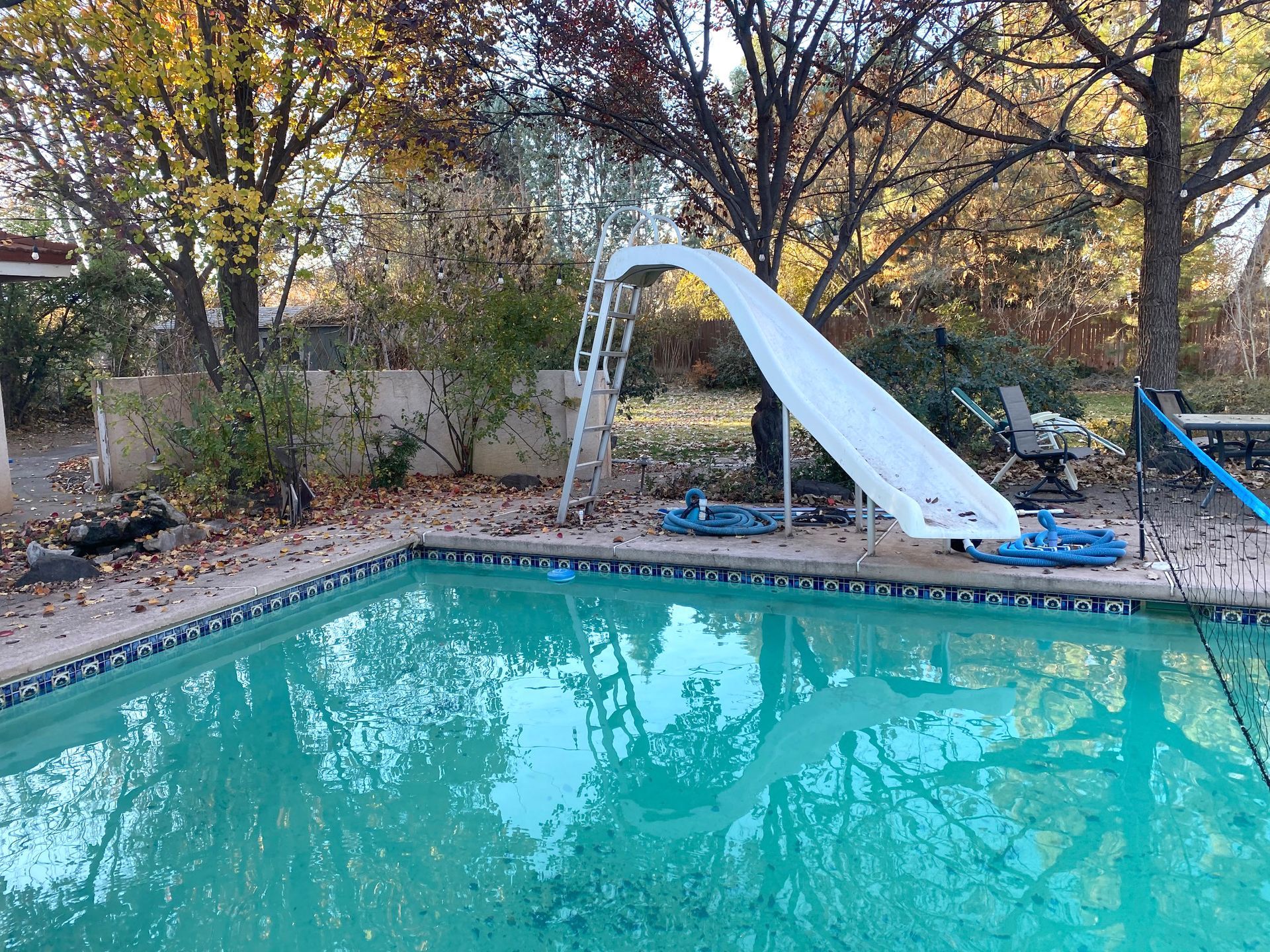 Swimming pool with slide, surrounded by trees with fall foliage.