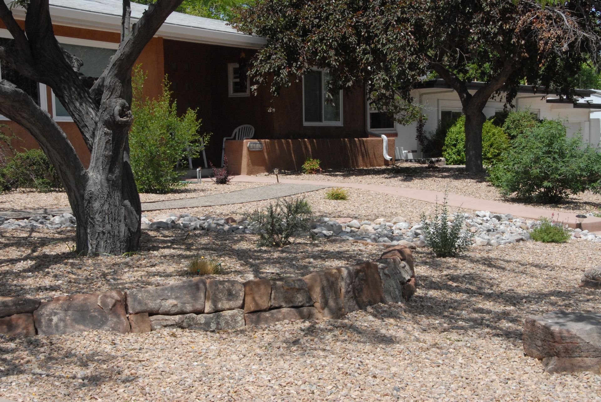 A brown house with a gravel yard, trees, and rock retaining walls.