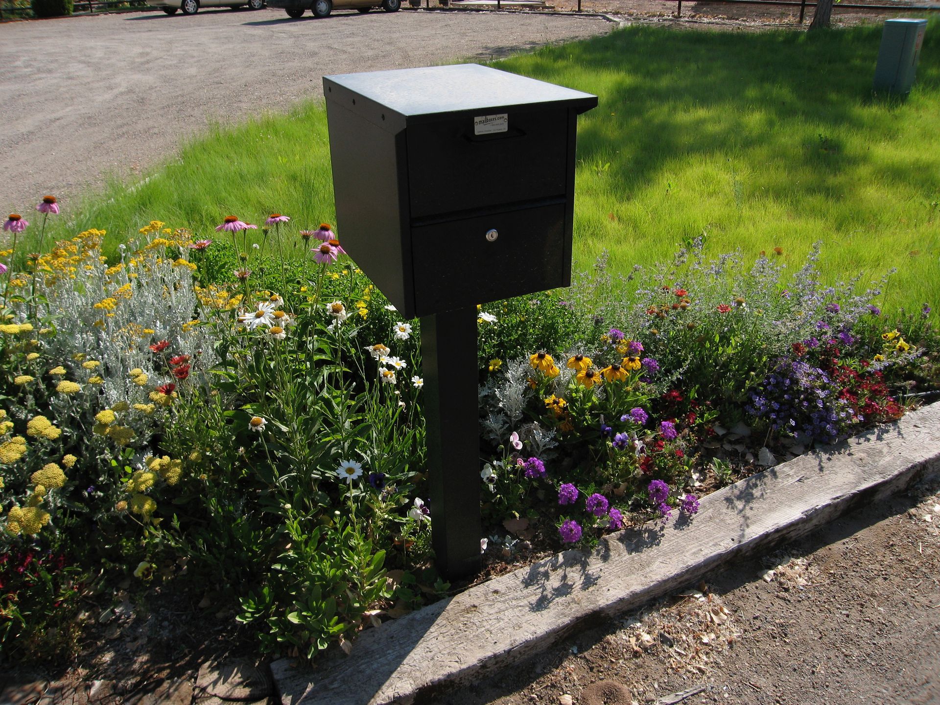 Black mailbox on post next to a flowerbed.
