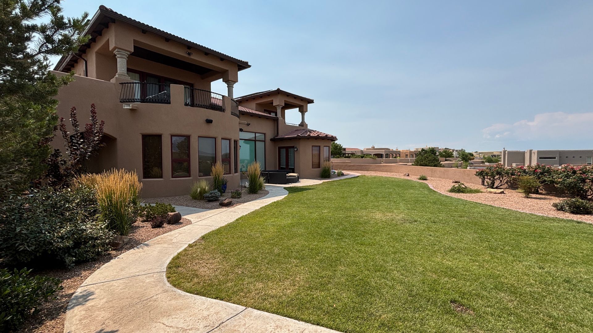 Beige stucco home with a green lawn and a pathway.