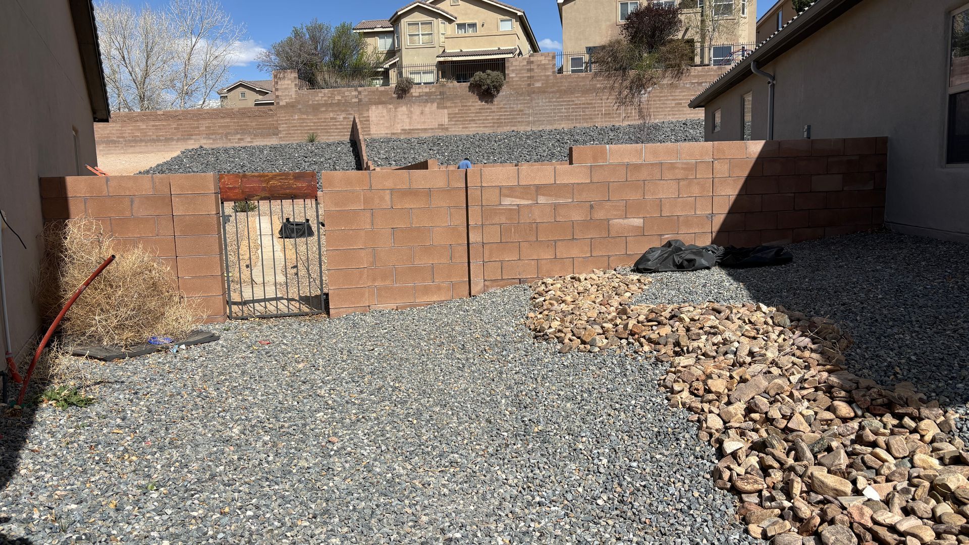A small backyard with a brick wall, stone ground, and a wooden door, with a hillside in the background.