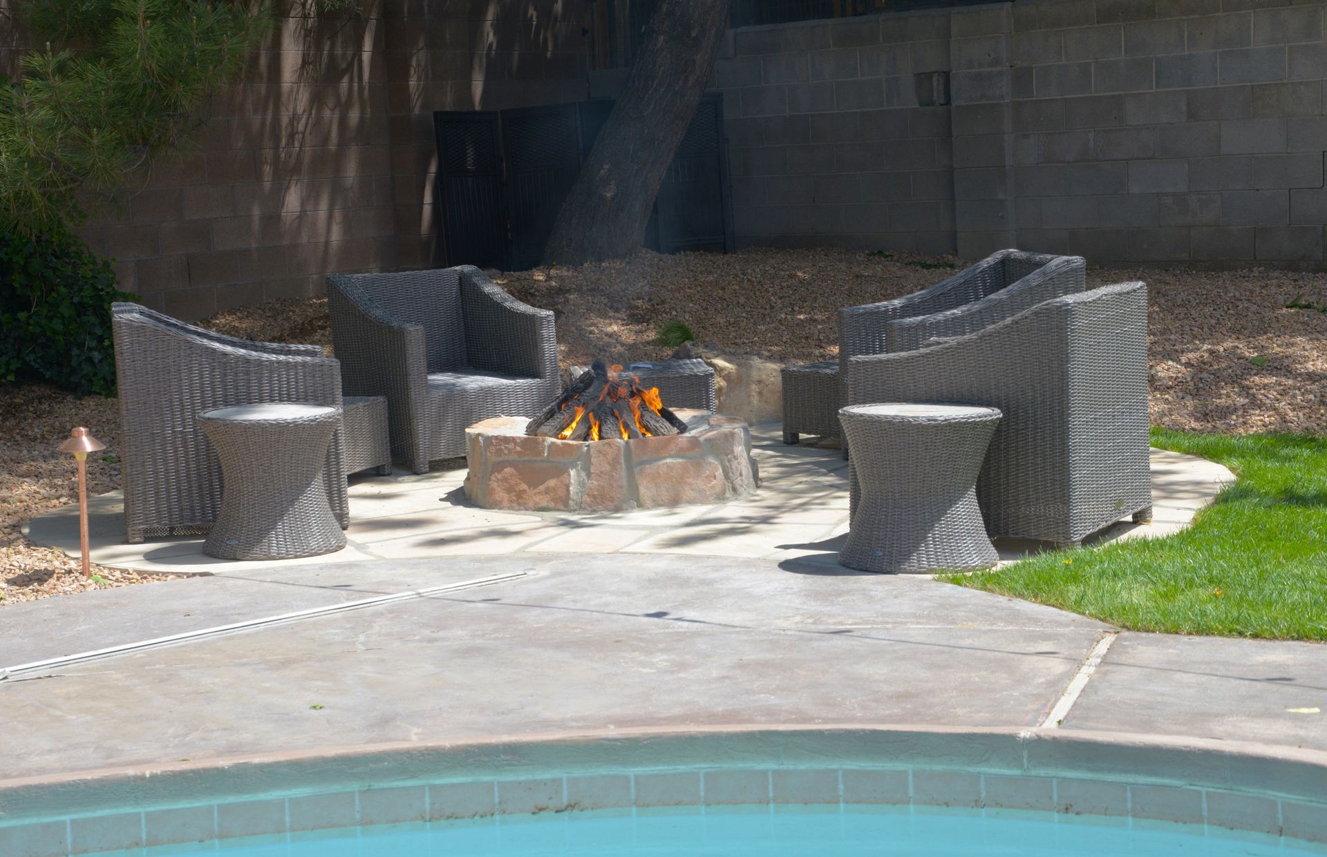 Outdoor seating area with fire pit, dark woven chairs, and small tables near a pool.
