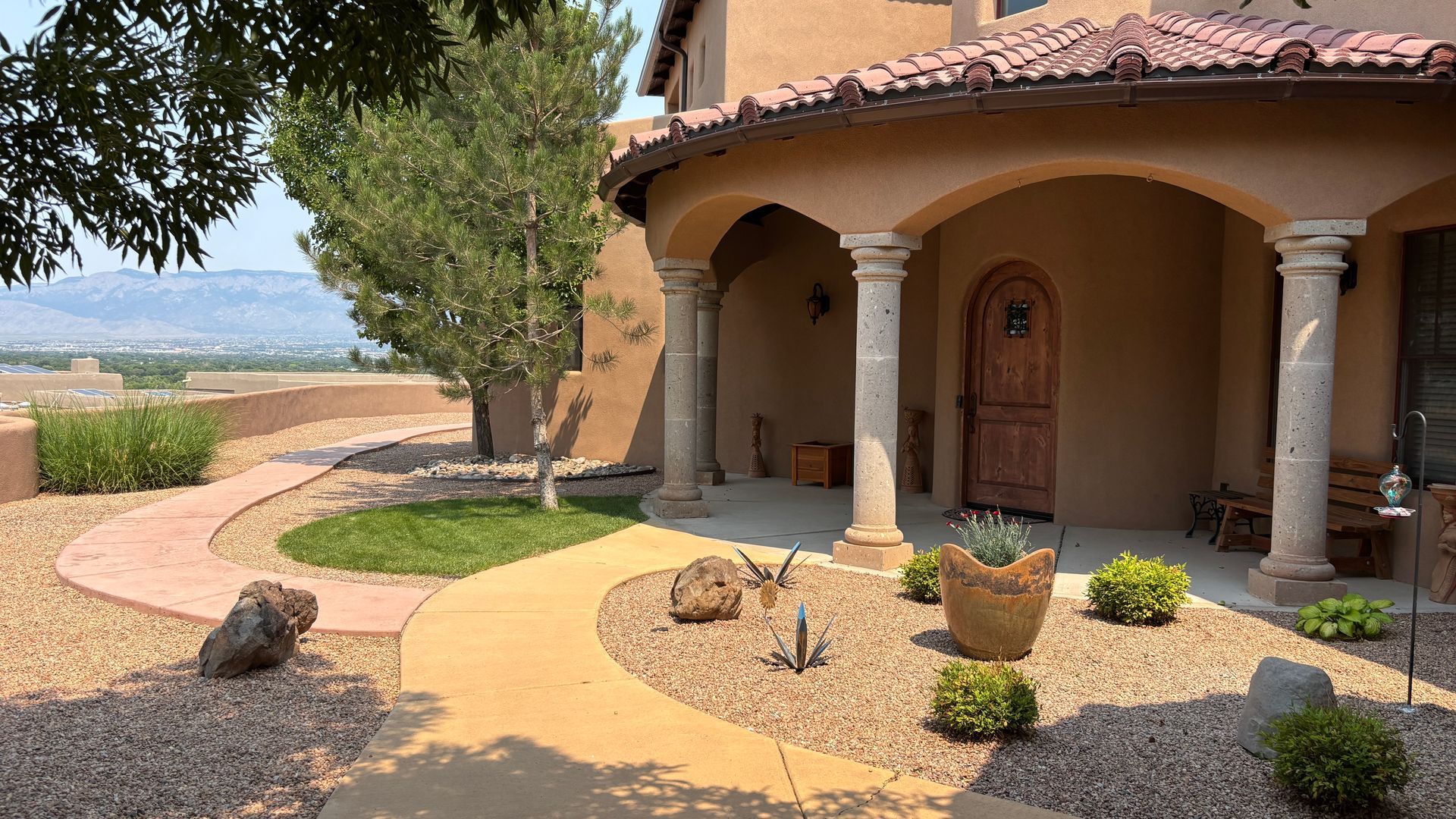 A tan stucco home with a curved entry, columns, and a path lined with rocks and small shrubs.