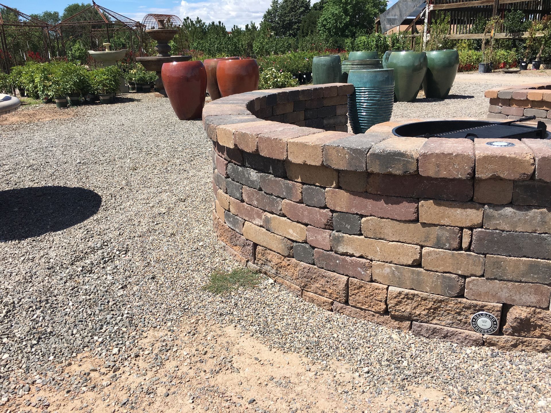 Fire pit built of bricks, surrounded by gravel, with terracotta pots in the background.