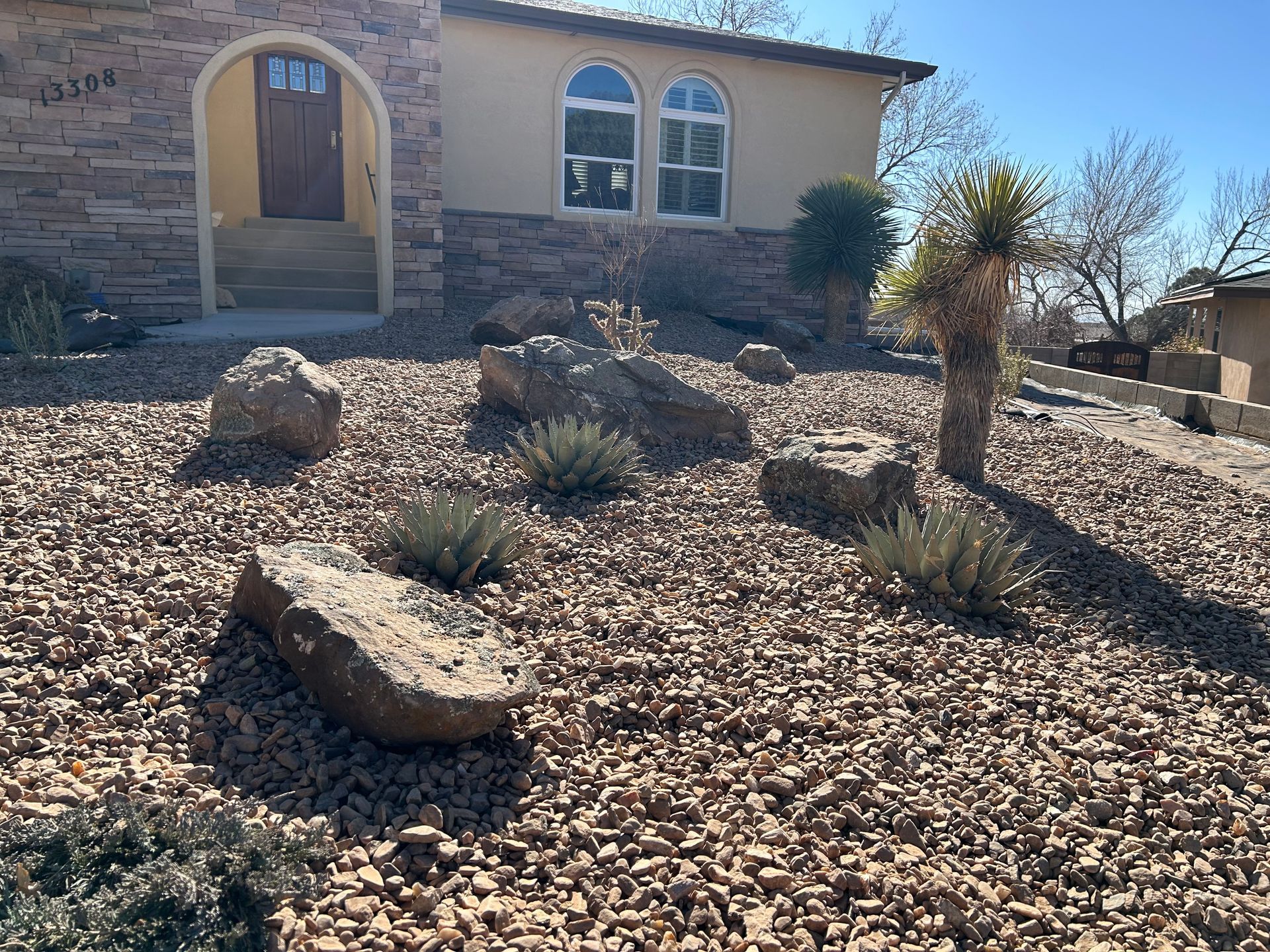 Tan house with stone facade and rock landscaping, with boulders, succulents, and gravel.