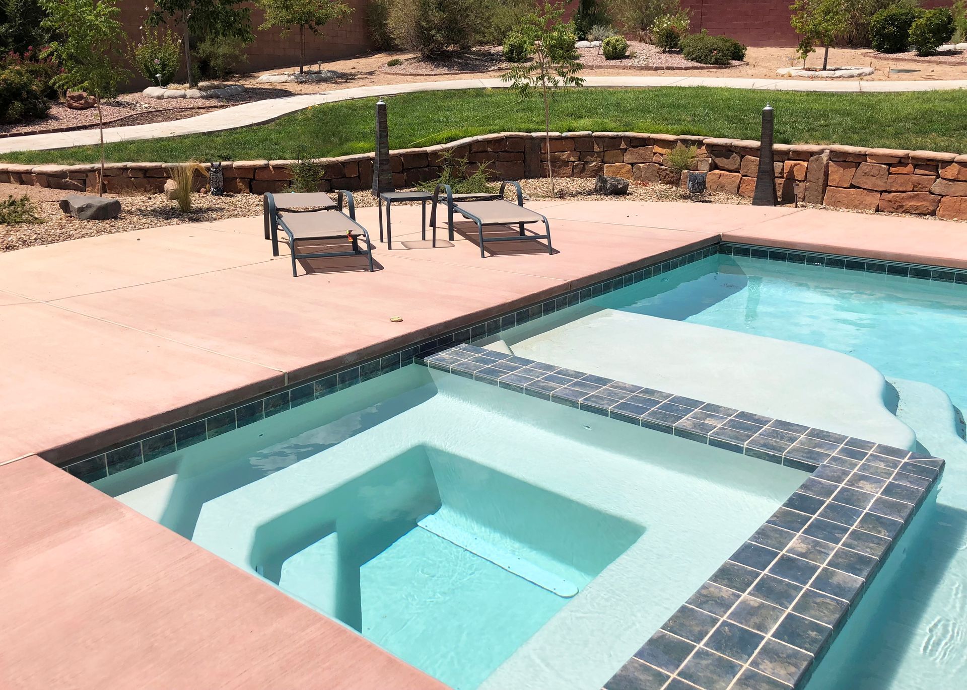Pool with steps, lounge chairs on a red patio, and green lawn in the background.