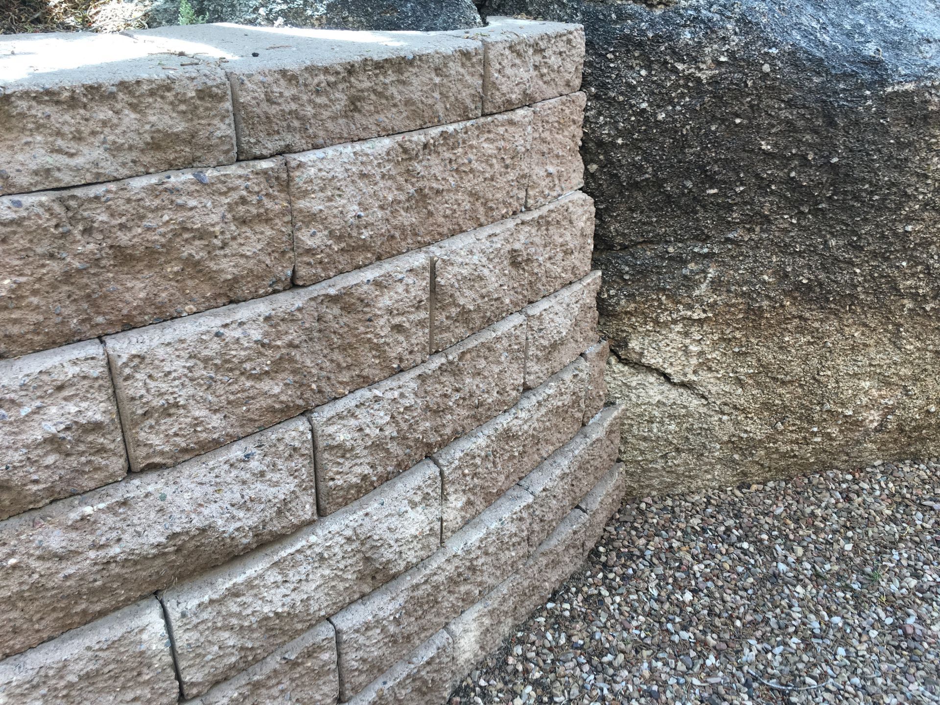 Tan retaining wall with a curved corner next to gravel and a rock face.