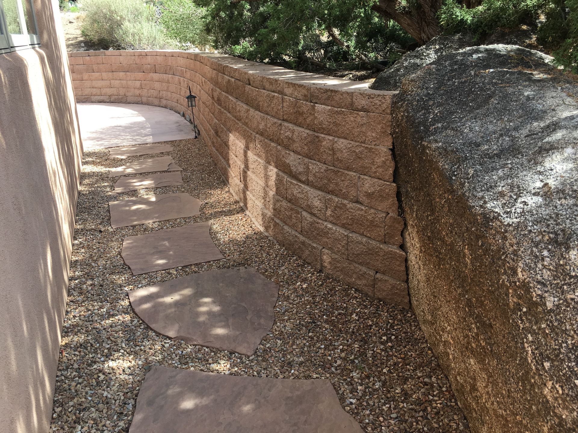 Stone pathway with stepping stones, bordered by a retaining wall and large rock.