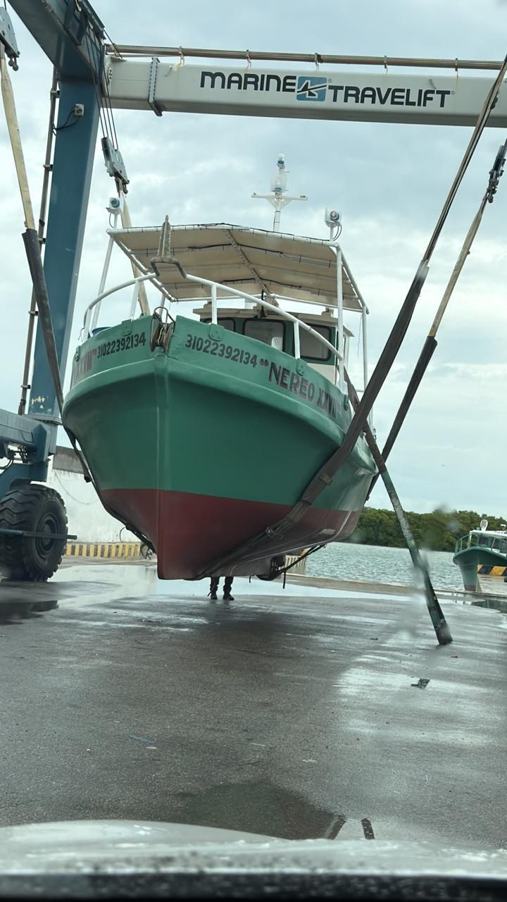 Large green boat hoisted in a boatyard under a metal frame, with wet pavement below
