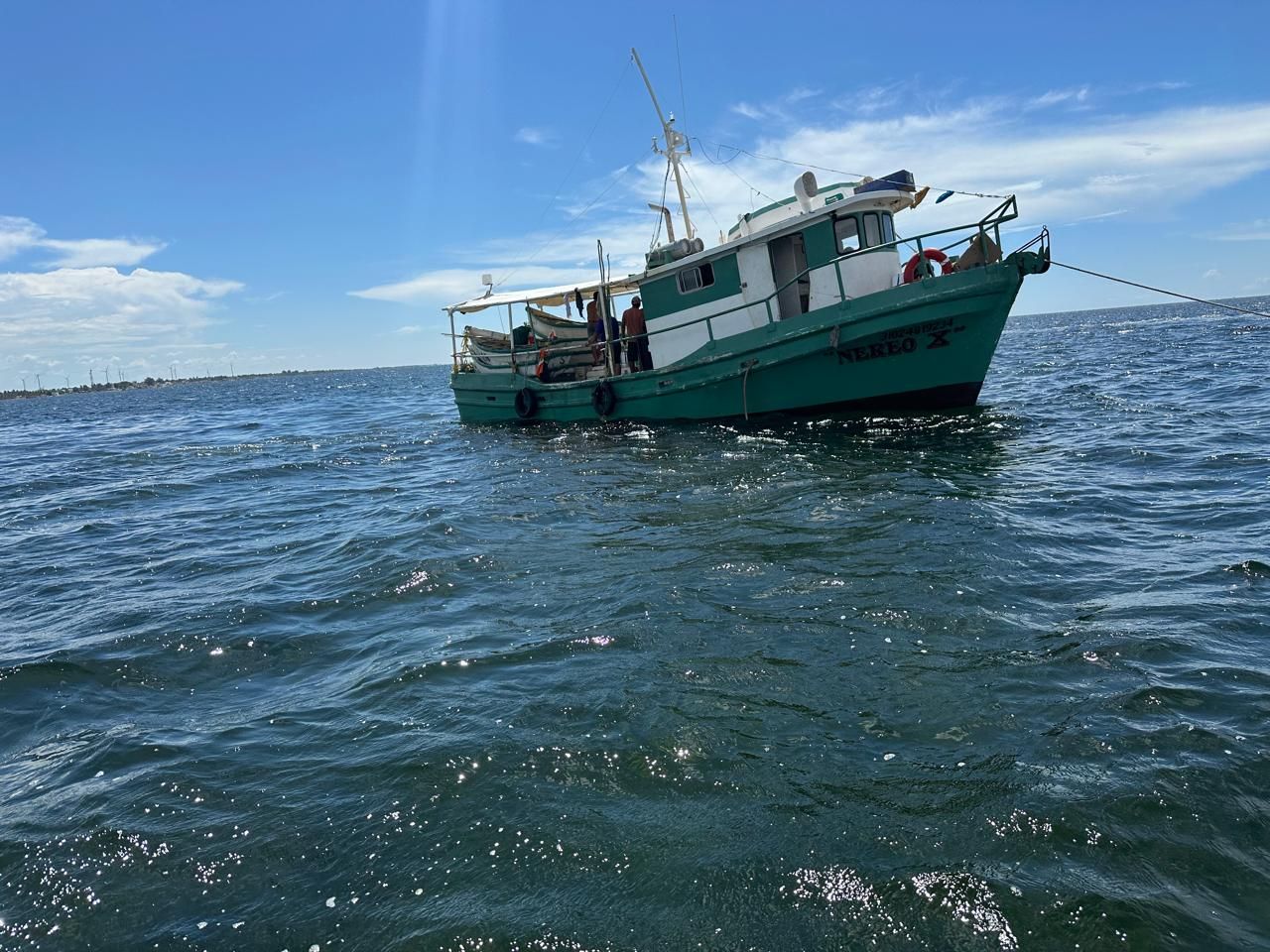 Green fishing boat on choppy blue water near a distant shoreline