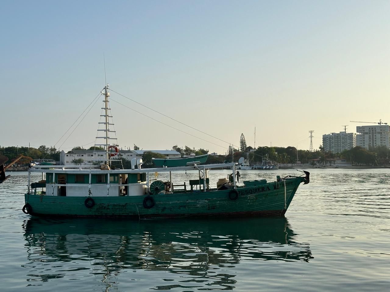 Green boat on calm water at sunset with city buildings in the background