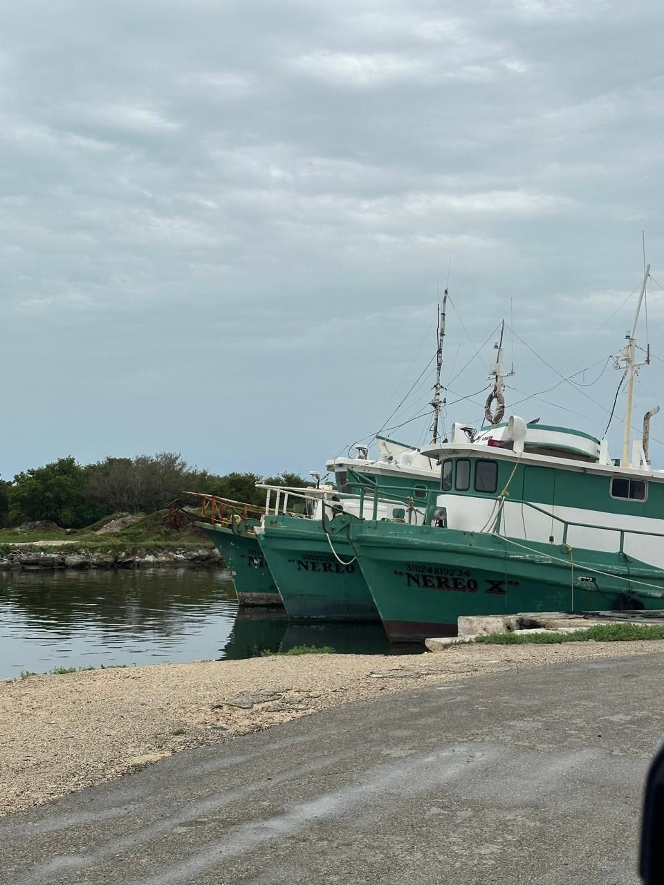 Two teal fishing boats docked on a rocky shore under a cloudy sky