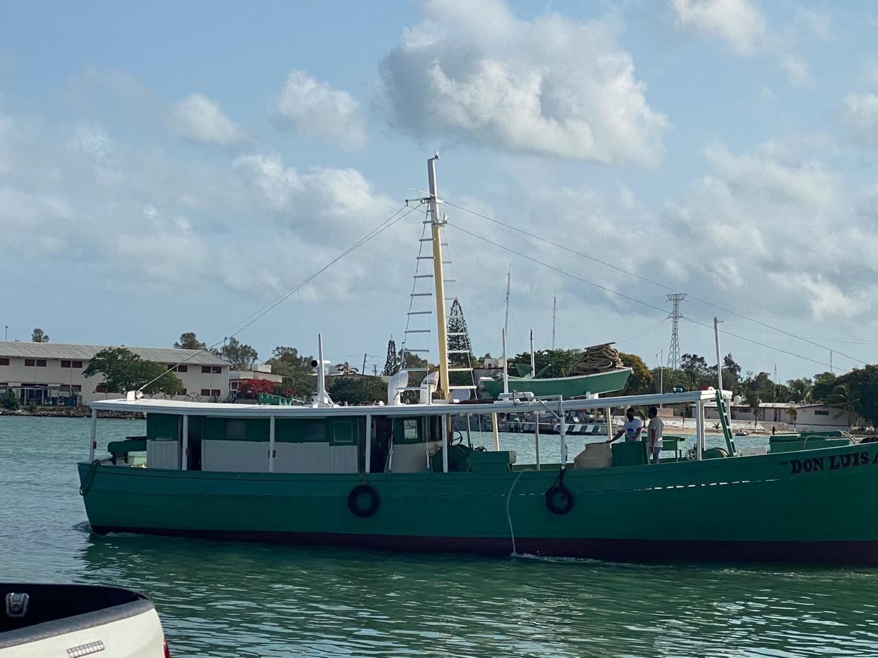 Green boat on calm water near a harbor under a cloudy sky