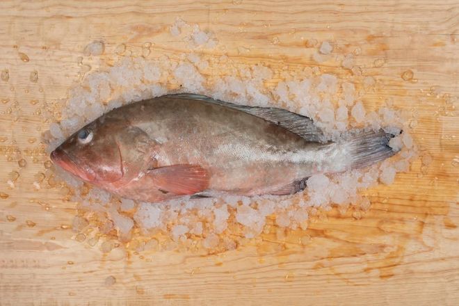 Whole fish lying on a wooden board with orange stains around it