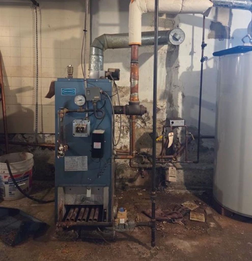 Boiler room with blue industrial furnace, pipes, gauges, and a large white tank on the right.