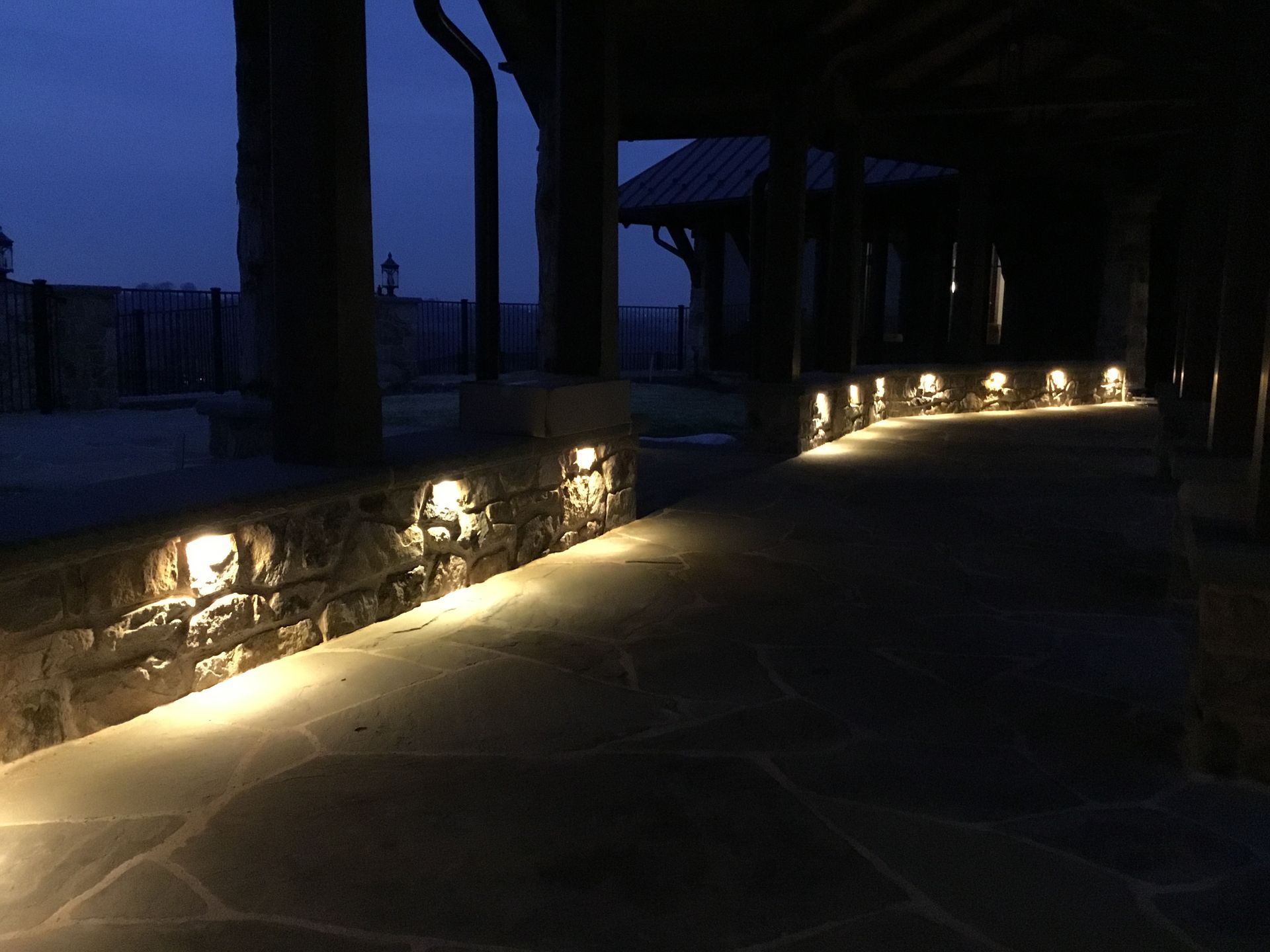 A stone walkway with lights on the side of it at night.