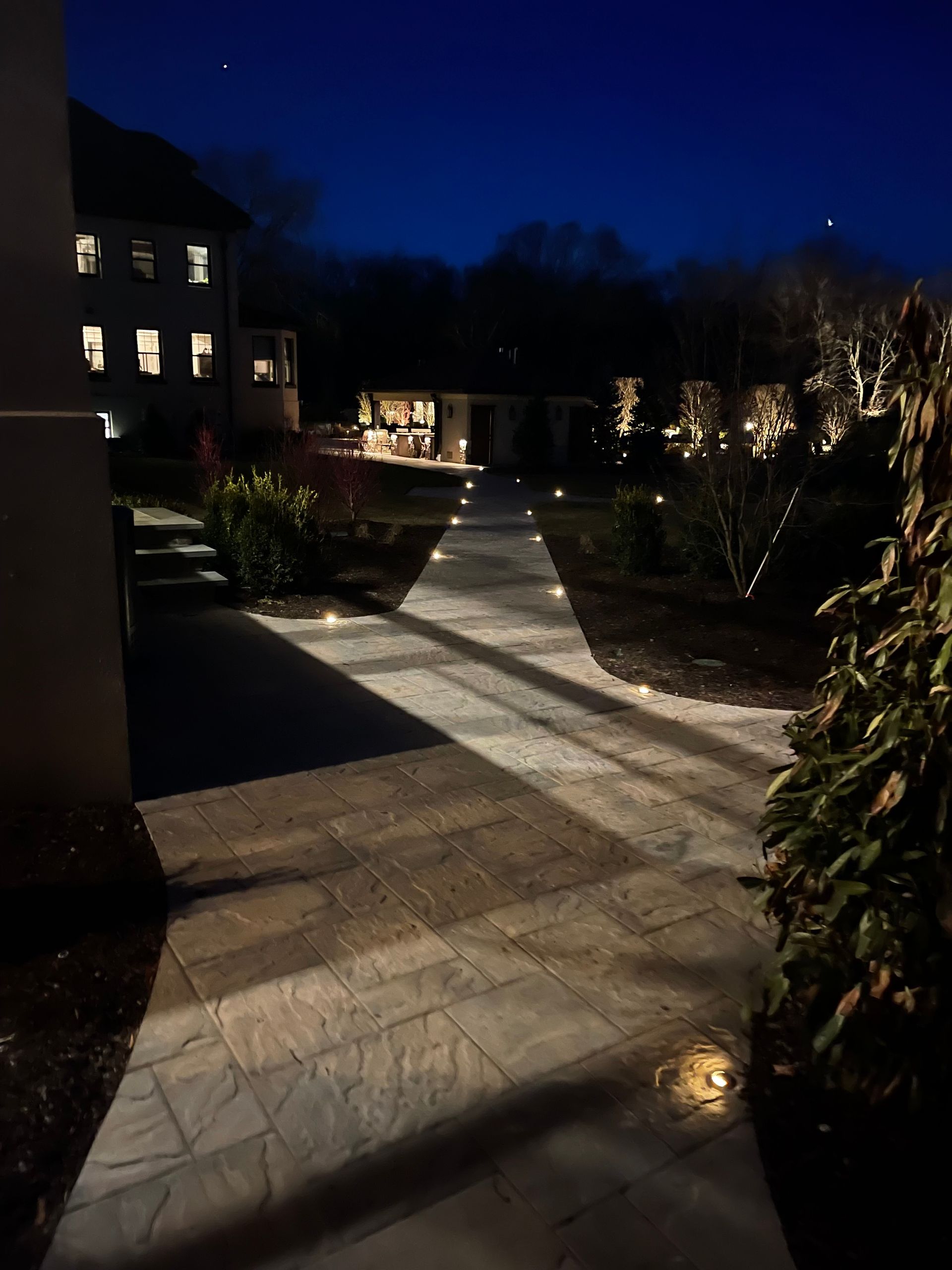 A walkway is lit up at night with a house in the background.