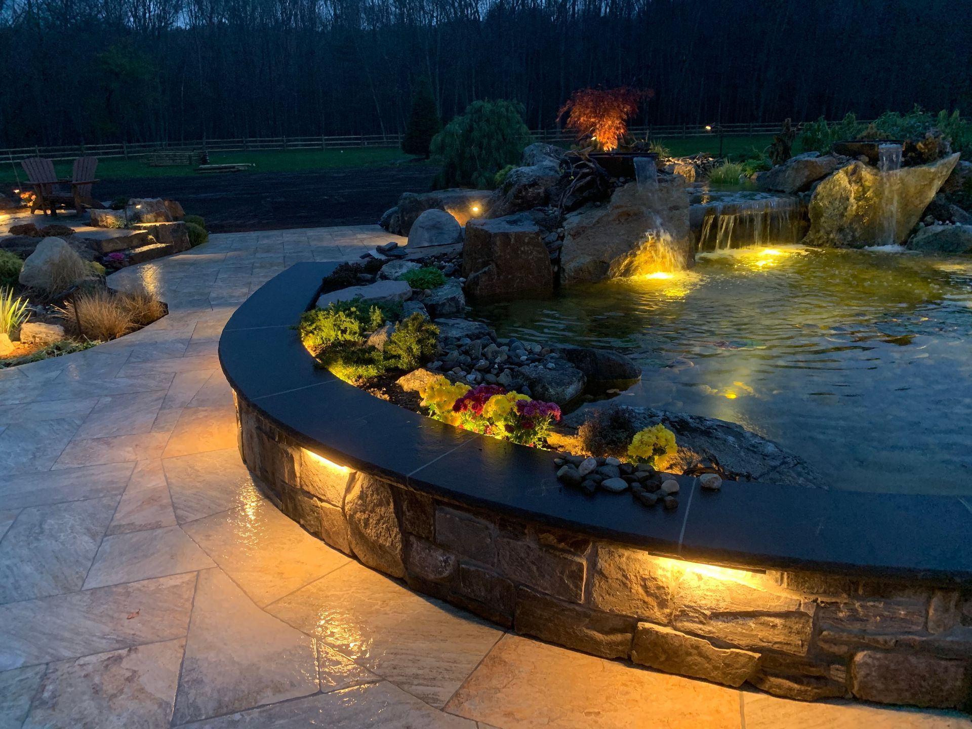 A pond with a waterfall in the middle of it is lit up at night.